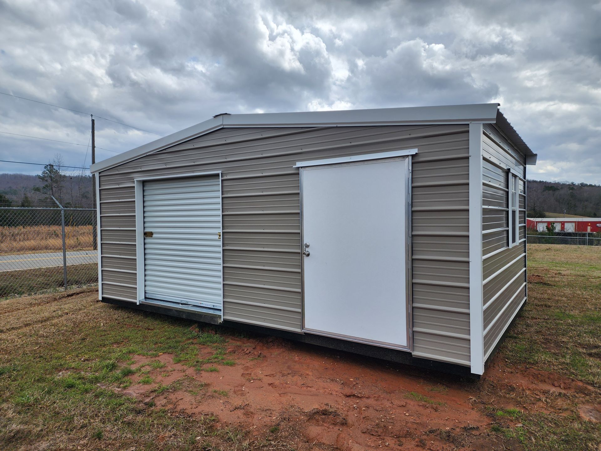 A metal shed with a white door is sitting in the middle of a field.