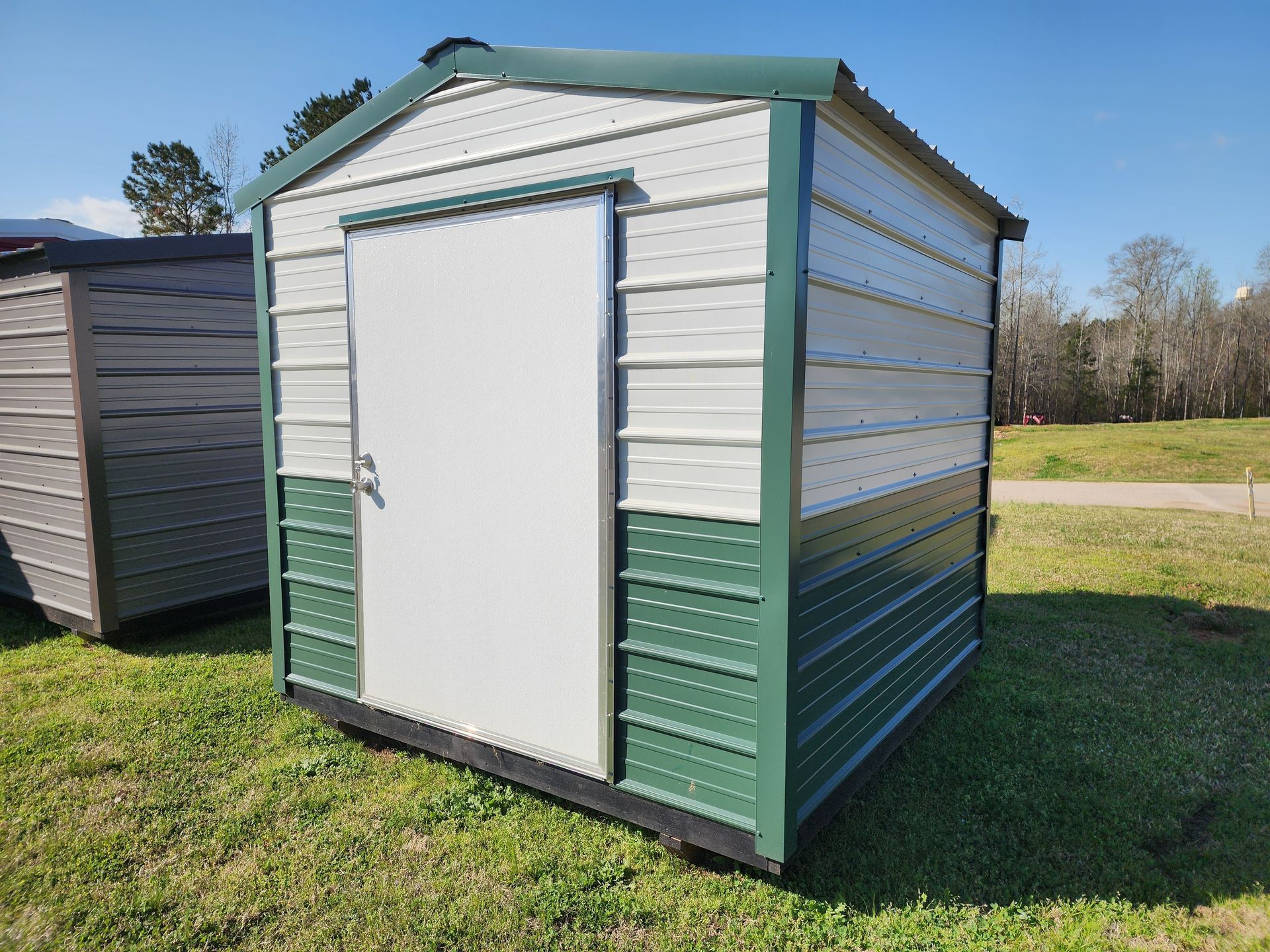 A green and white shed with a white door is sitting in the grass.