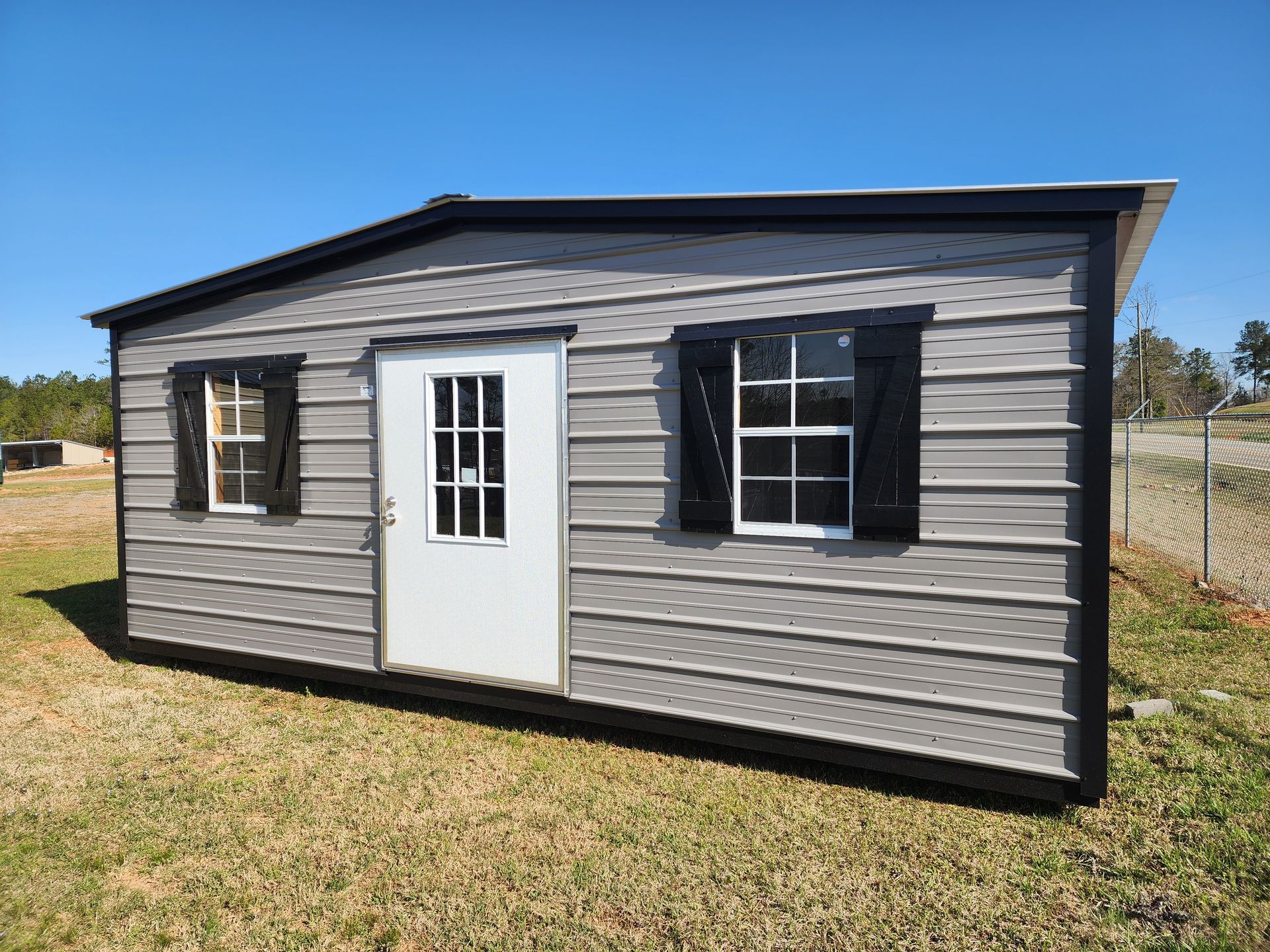 A small house with a white door and windows is sitting in the middle of a grassy field.