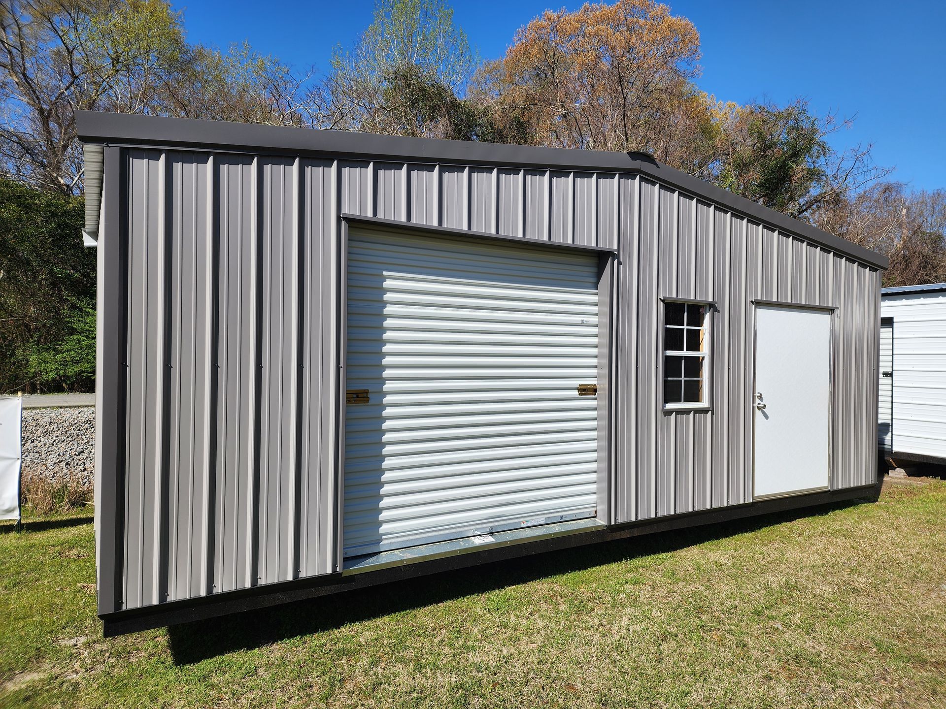 Gray metal shed with a garage door, a small window, and a door on green grass.