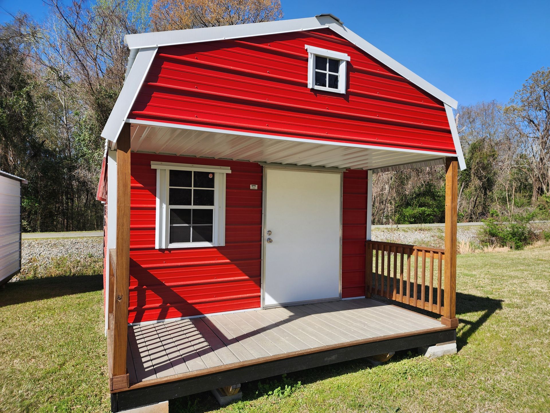 Red storage shed with a porch on a grassy lawn.