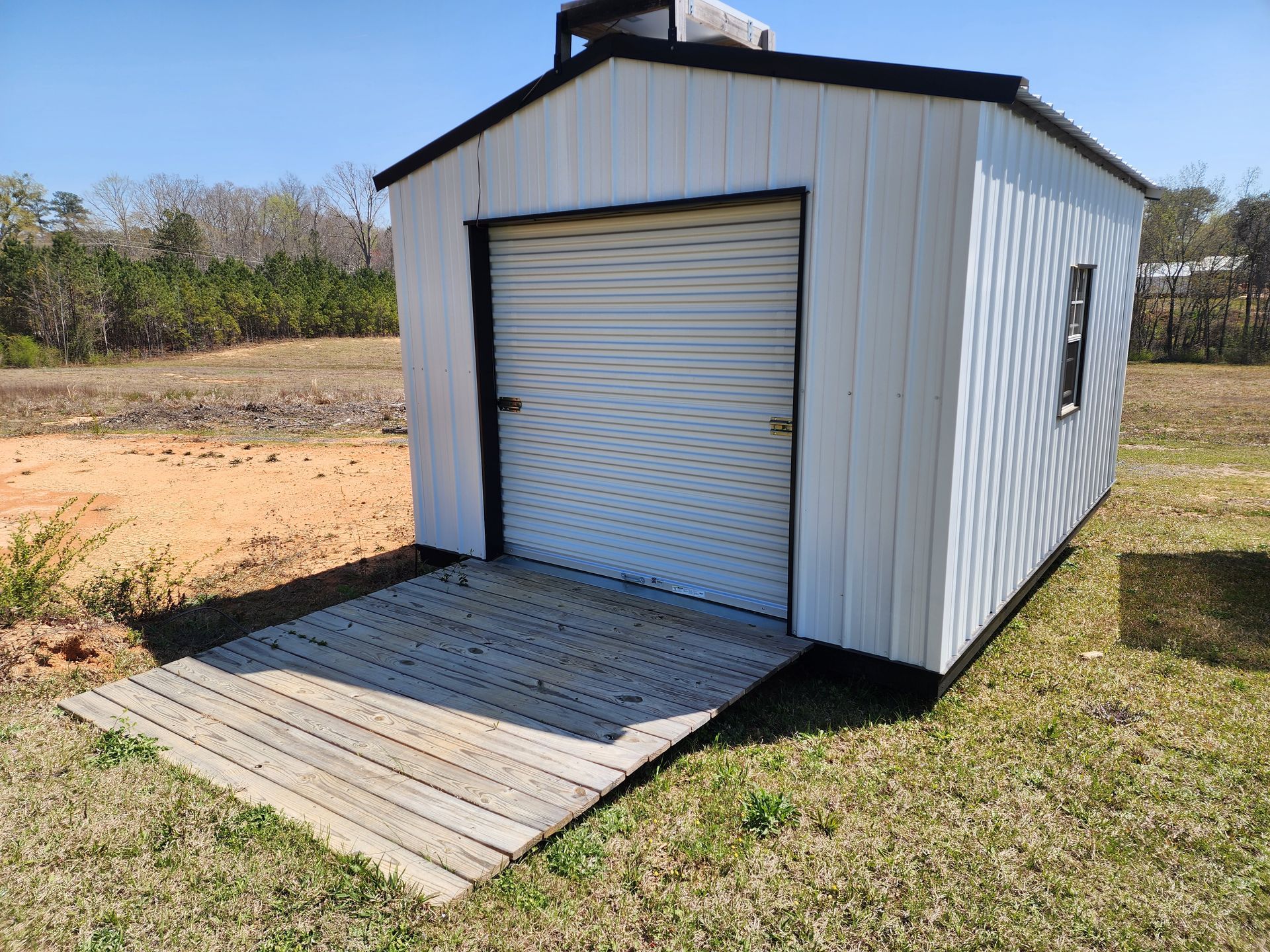 A white shed with a garage door is sitting in the middle of a grassy field.