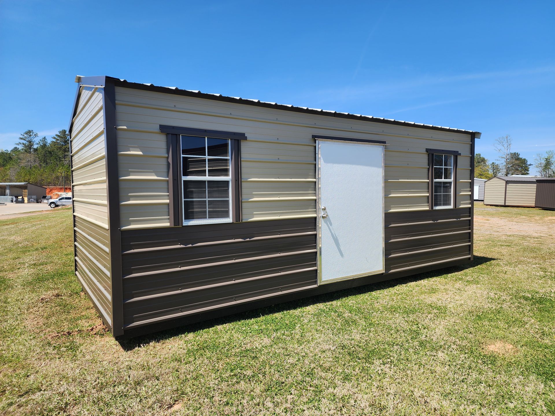A small shed with two windows and a door is sitting in the middle of a grassy field.