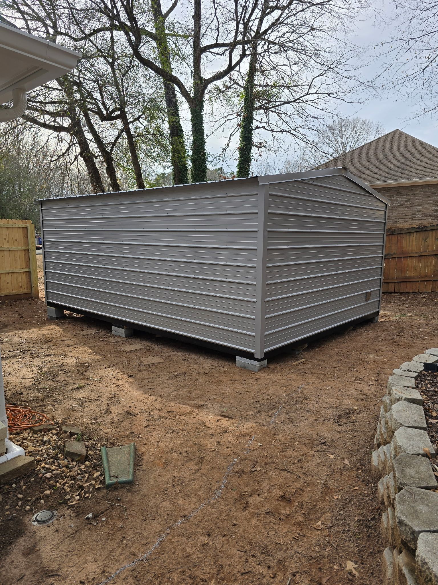 Gray metal storage shed in a yard, on concrete blocks.