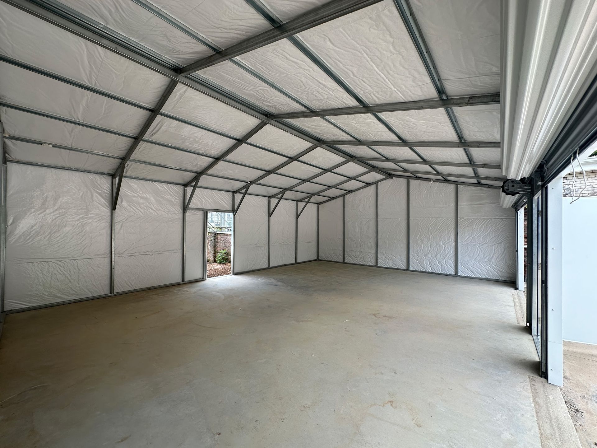 Interior of a large, empty metal building with a concrete floor, insulated walls, and a roller door.
