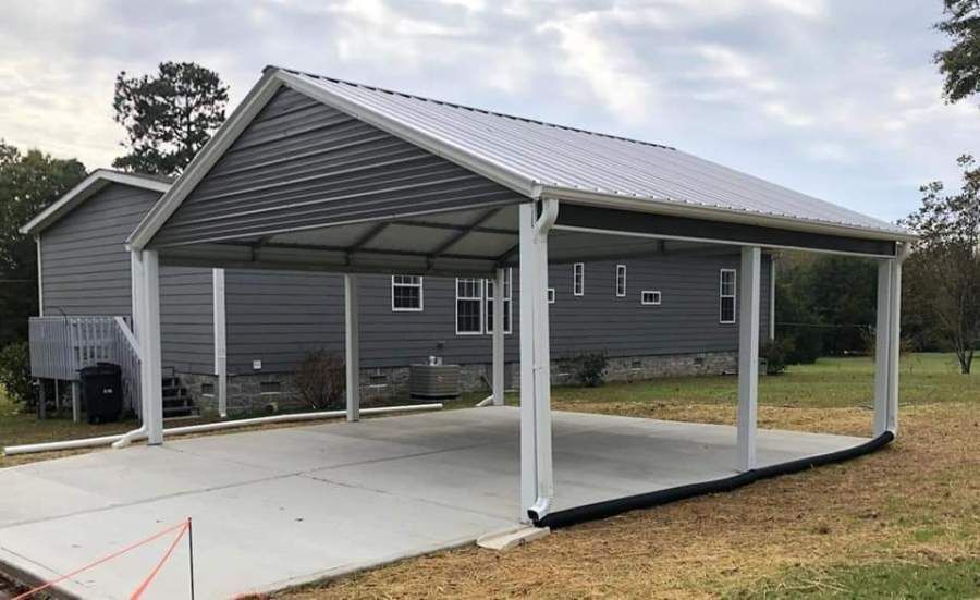 Carport with white roof, light gray siding, concrete floor, next to house, and green yard.