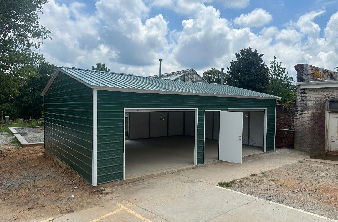 Green metal garage with white trim and open doors against a cloudy sky.