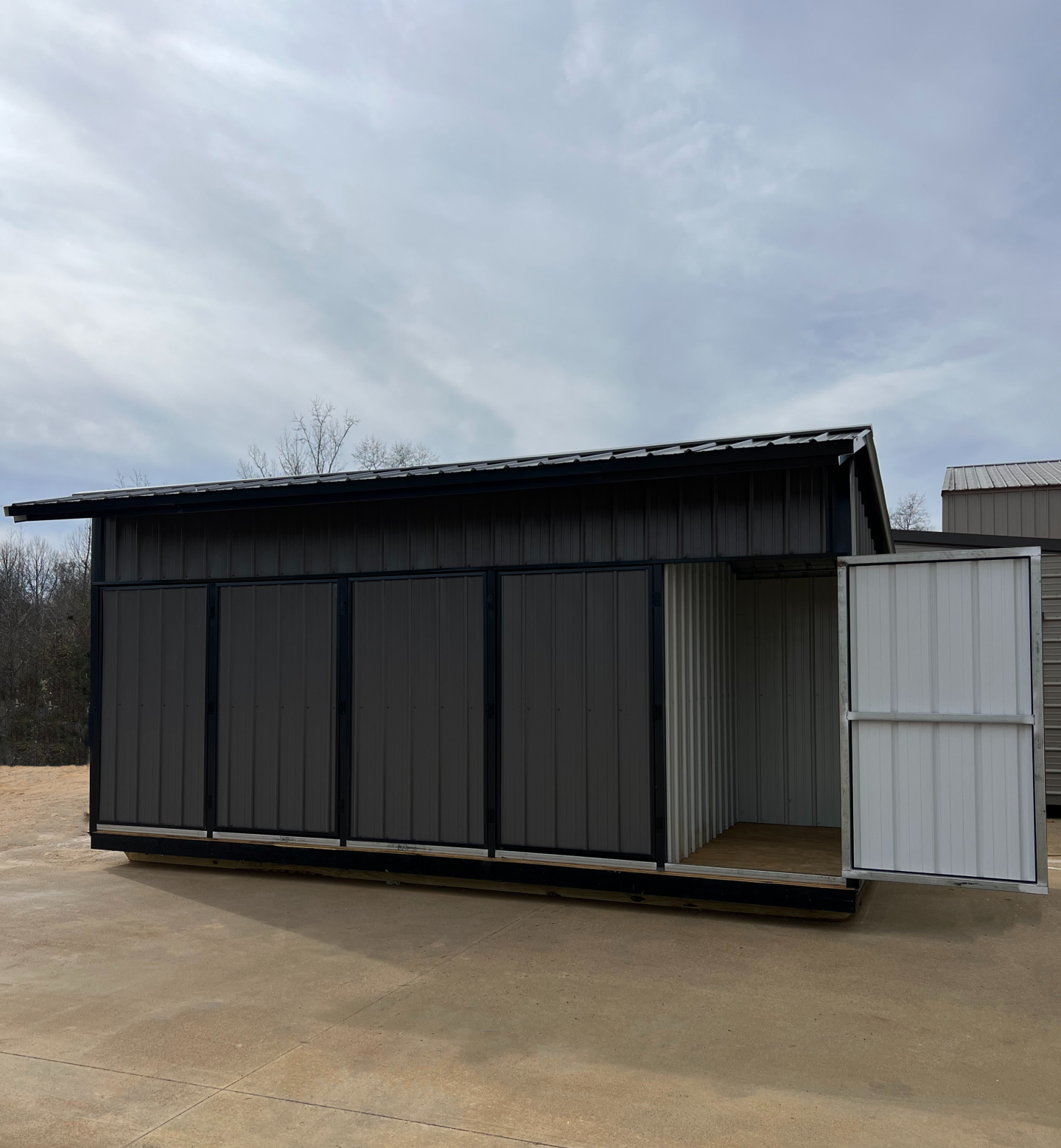 Gray metal storage shed with open white door, under a cloudy sky.