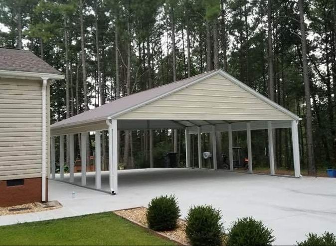 Carport attached to a house with concrete driveway, light beige siding, and white supports.