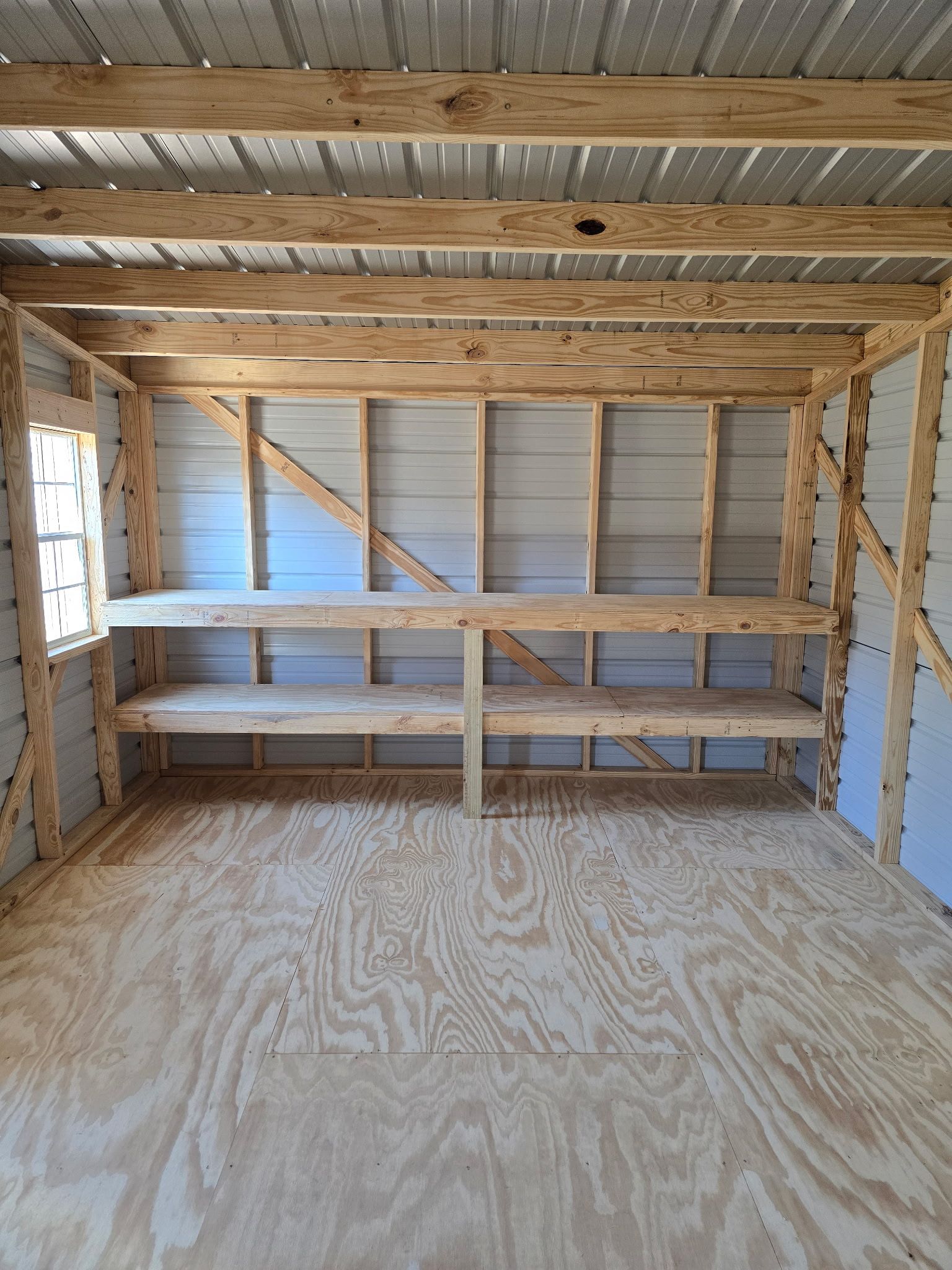 Interior of a shed with plywood floor and shelving, framed with wood, metal roof.