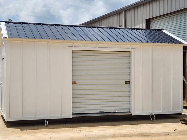 White storage shed with a roll-up door, sitting on wheels, with a dark roof.