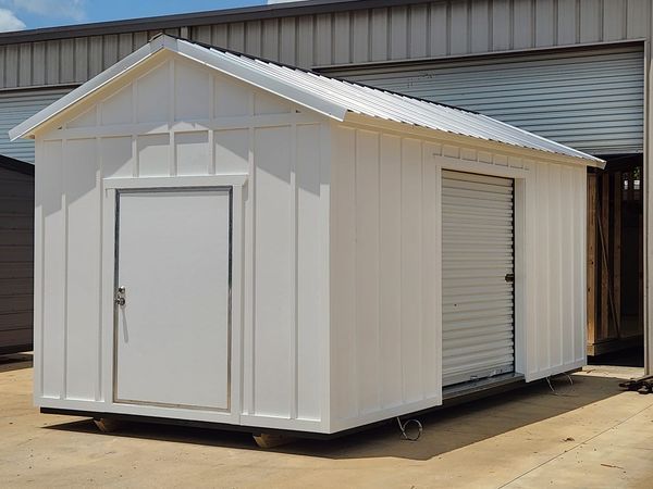 A white shed with a garage door is sitting in front of a building.