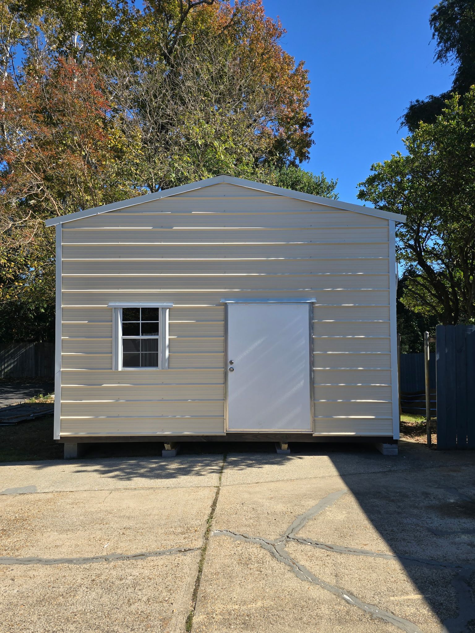 Beige metal shed with white door and window, set on concrete blocks.