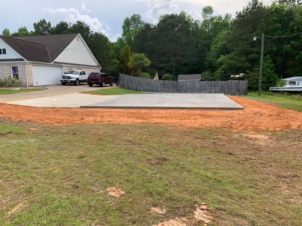 Concrete pad with cars in the driveway of a house. Dirt and grass surround the pad.
