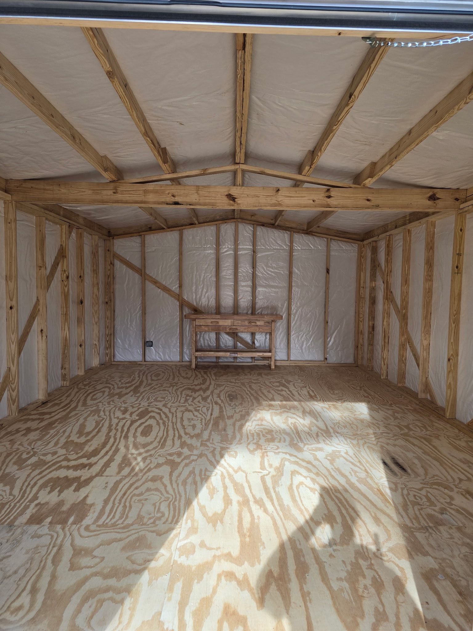 Interior of a wooden shed with a plywood floor and a small table centered against the back wall.