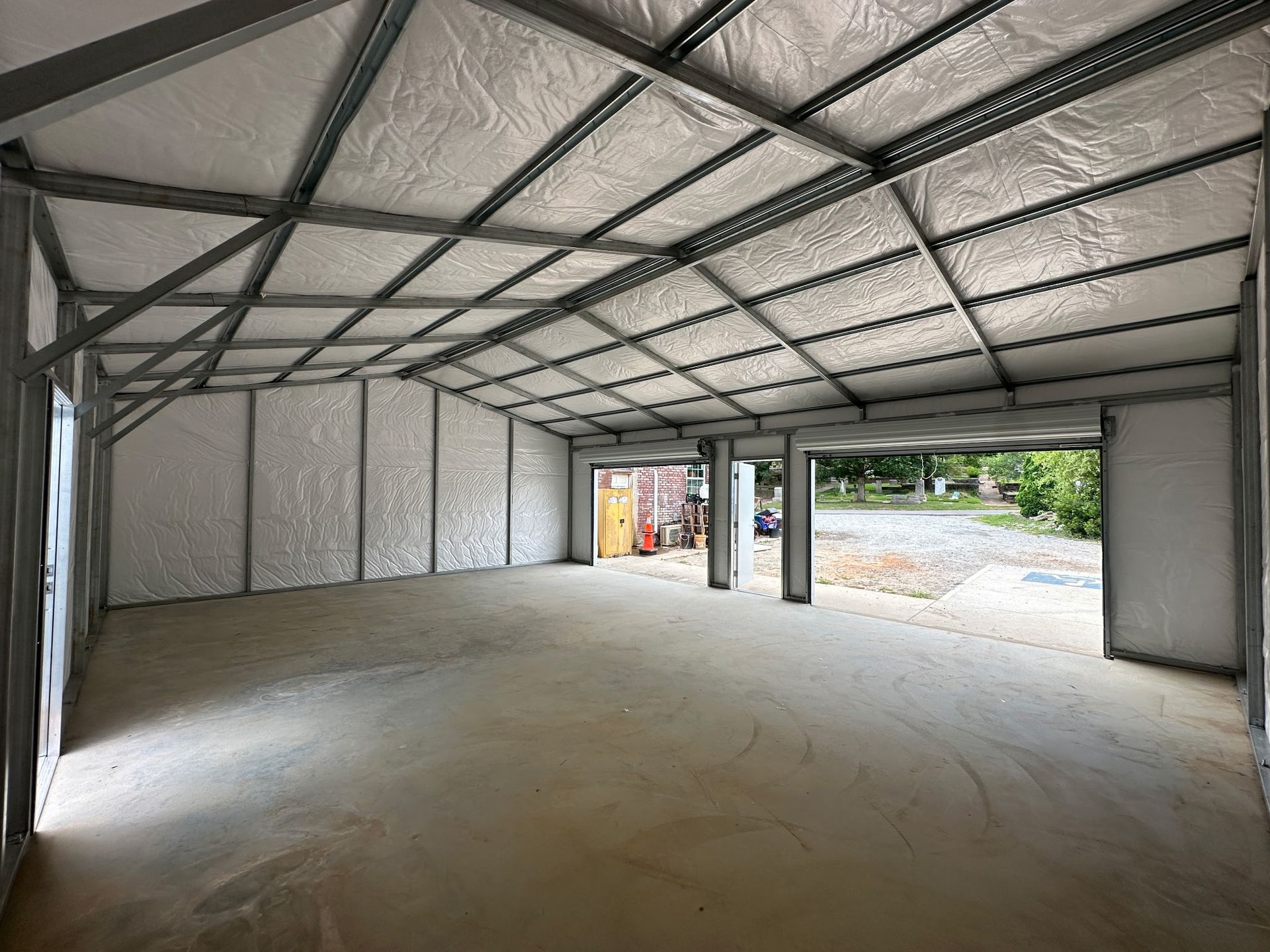 Interior view of a metal-framed building with a concrete floor, insulated walls and ceiling, and open garage door entrances.