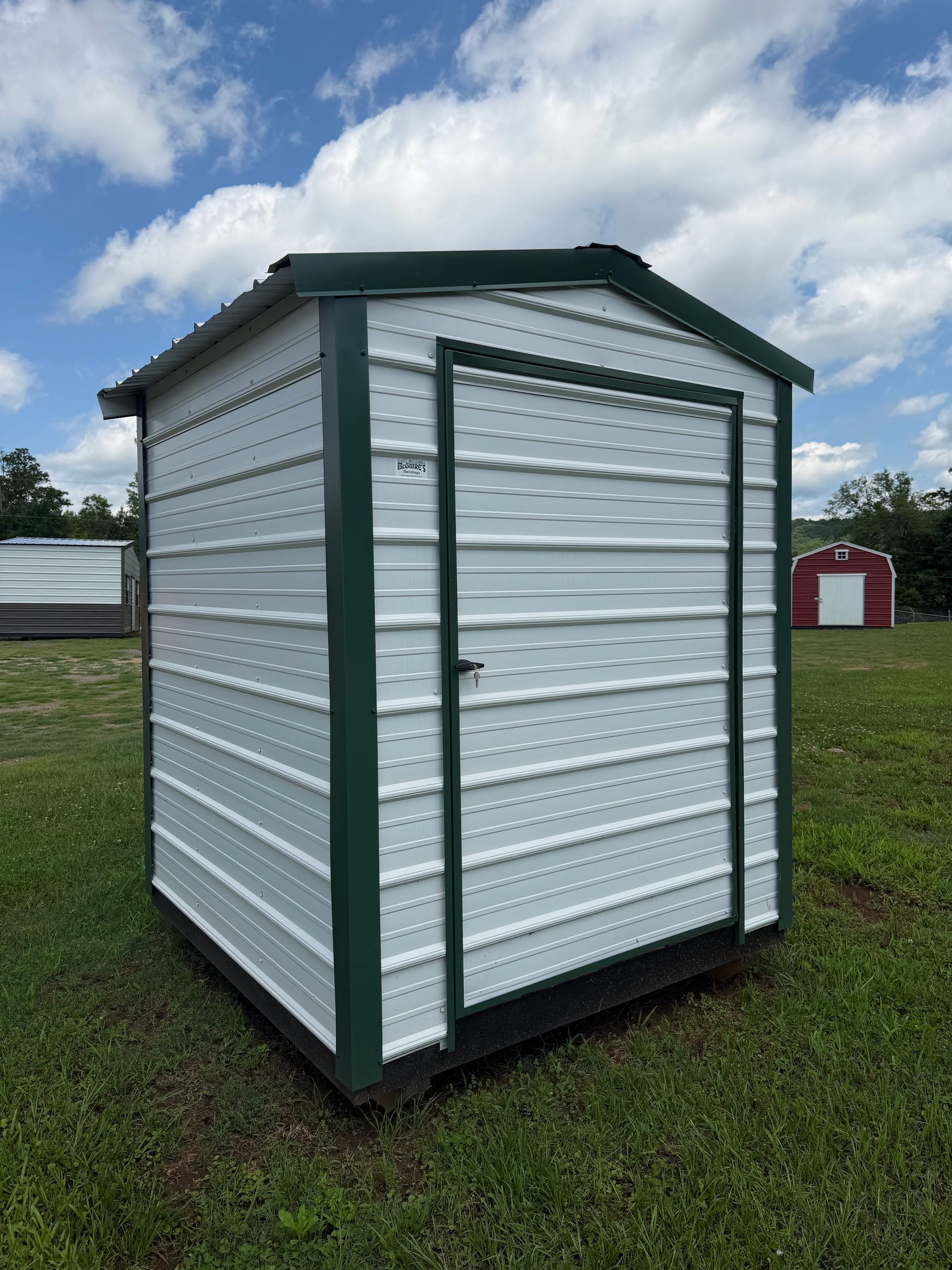 Small white shed with green trim standing on grass under a cloudy sky