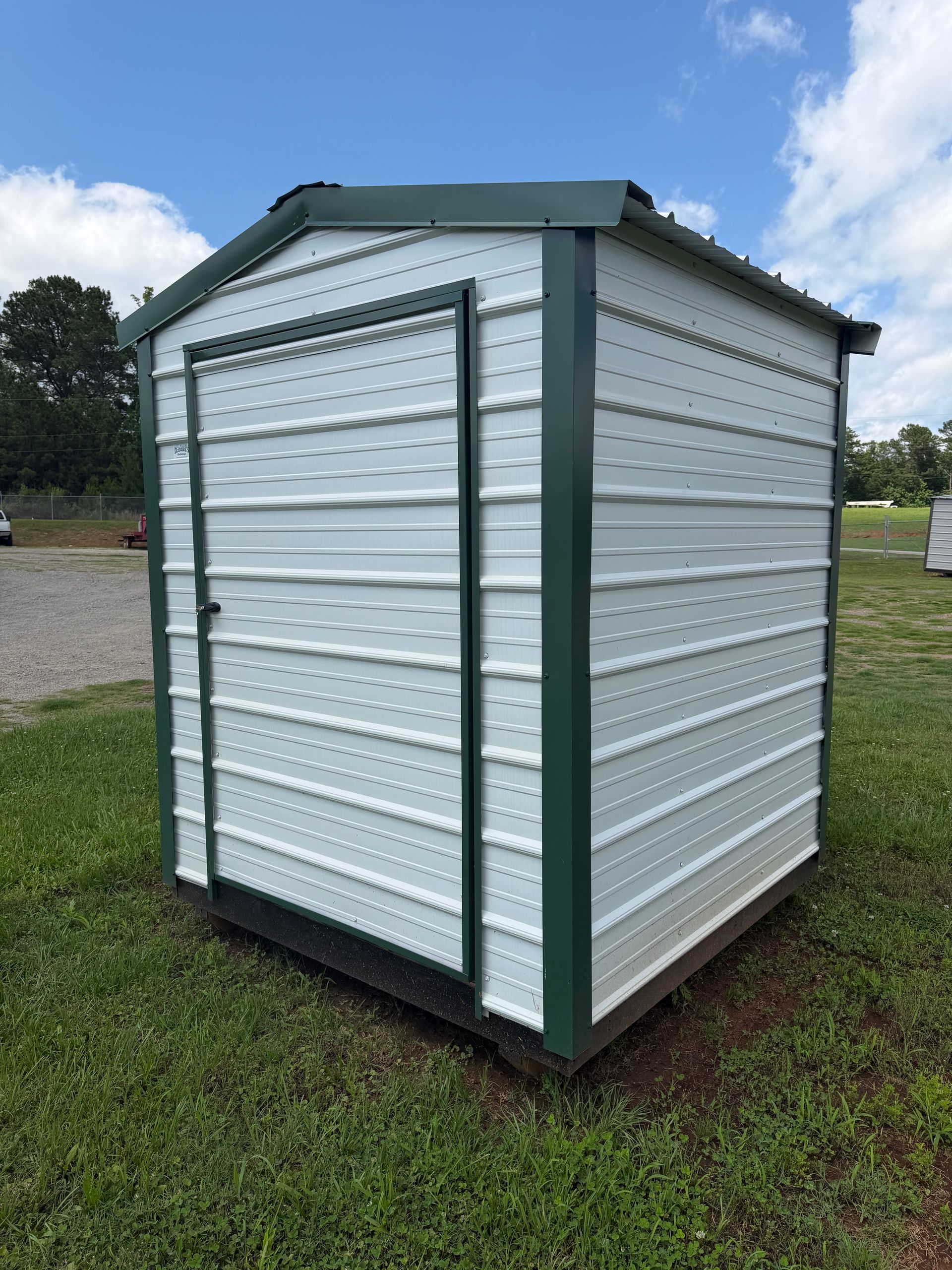 White metal storage shed with green trim on a grassy lot under a cloudy sky