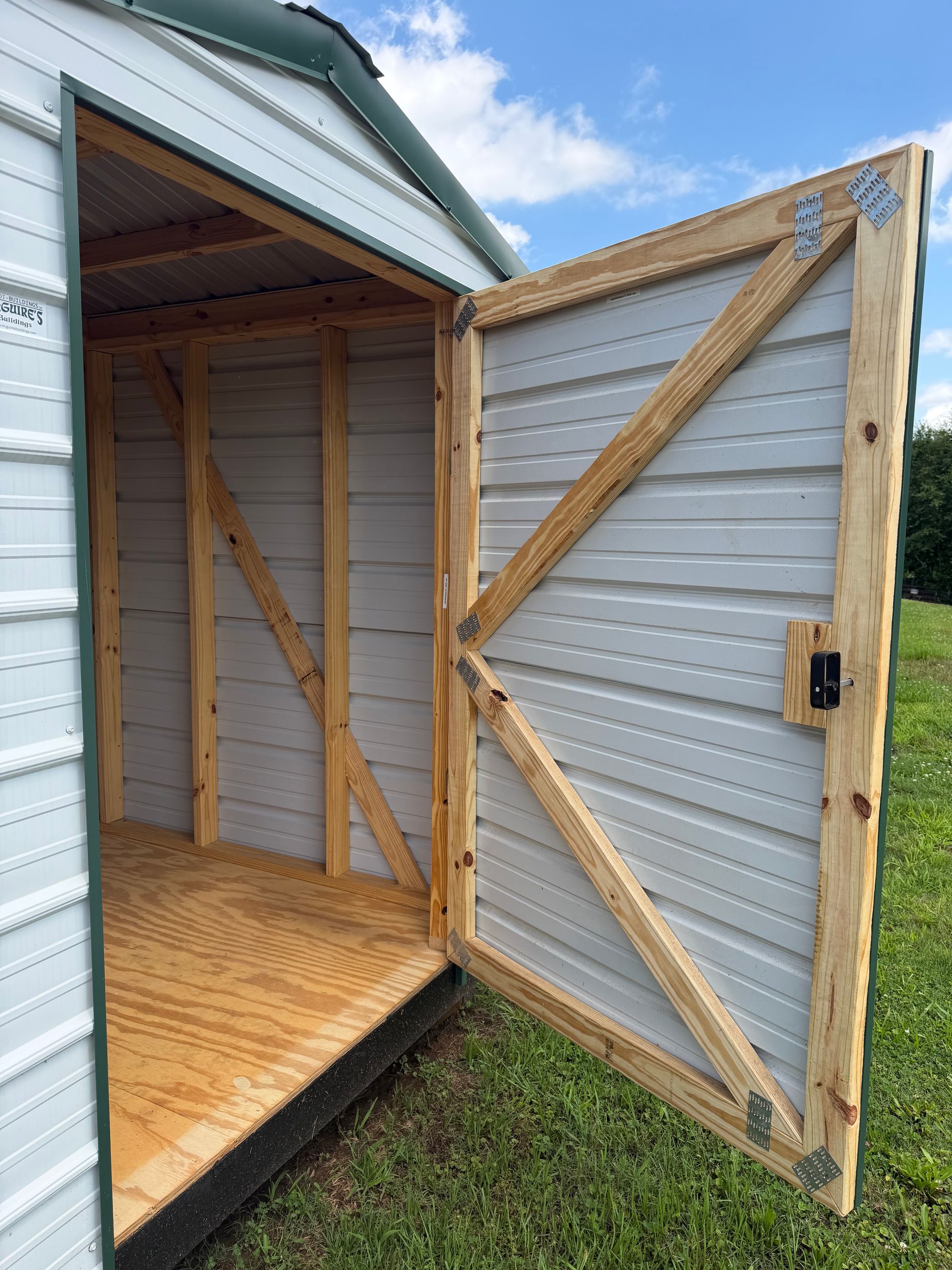 Open wooden shed door with diagonal bracing, showing the interior and wooden floor inside.