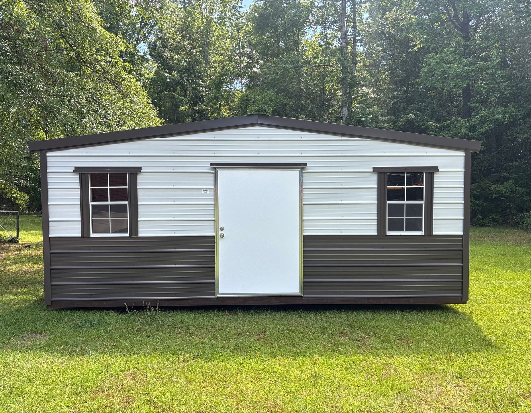 Metal shed with white and brown walls, two windows, and a door on a grassy lawn.