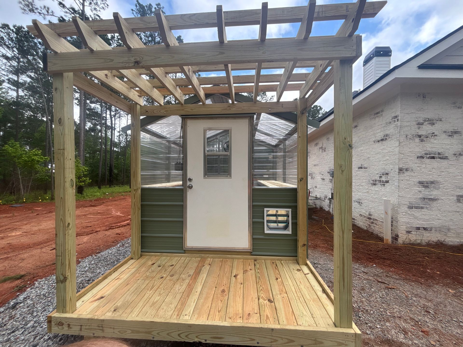Wooden structure with a door, greenhouse-like sides, and a pergola top; outdoors.