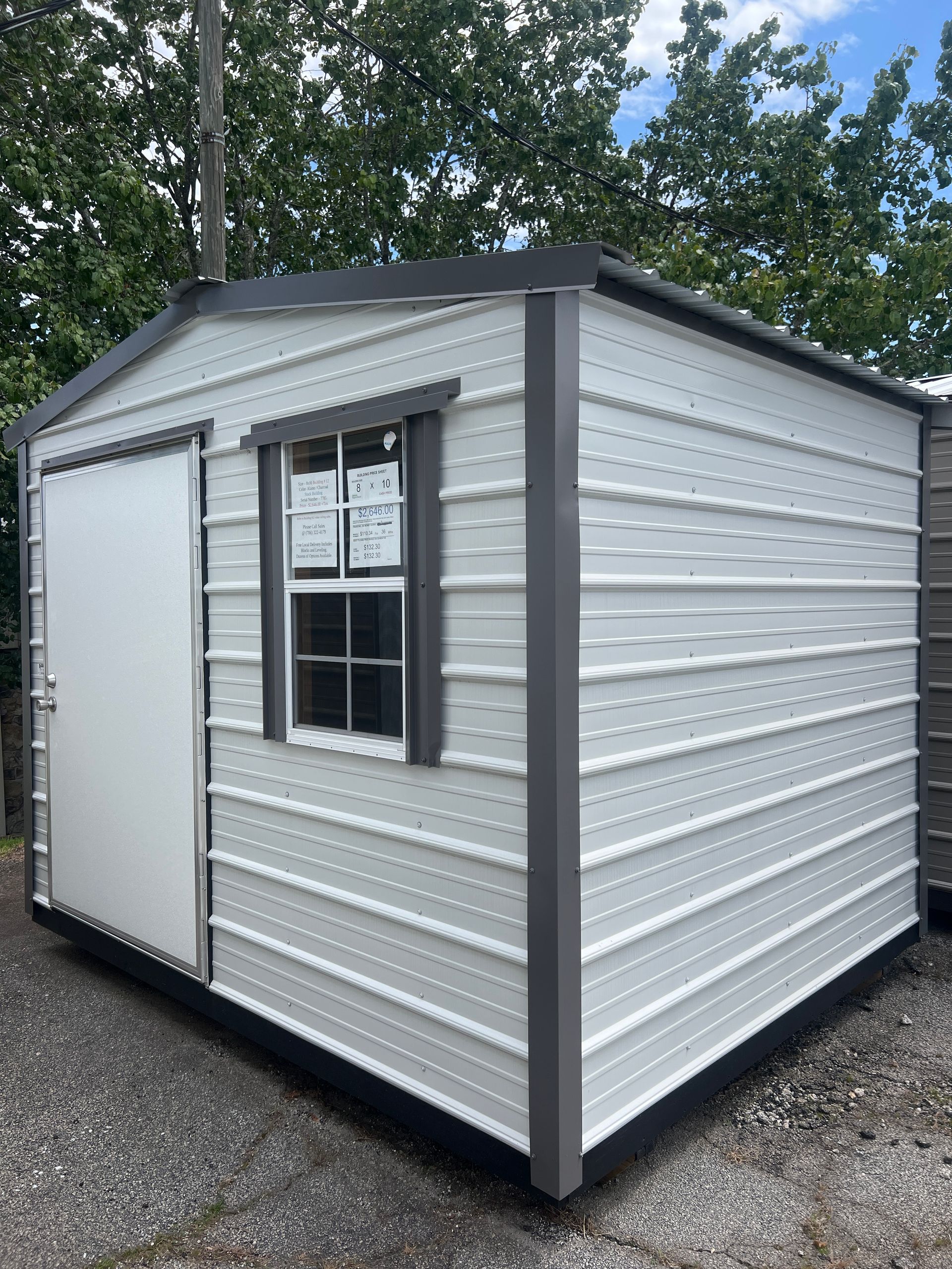White metal storage shed with a gray frame, door, and window.