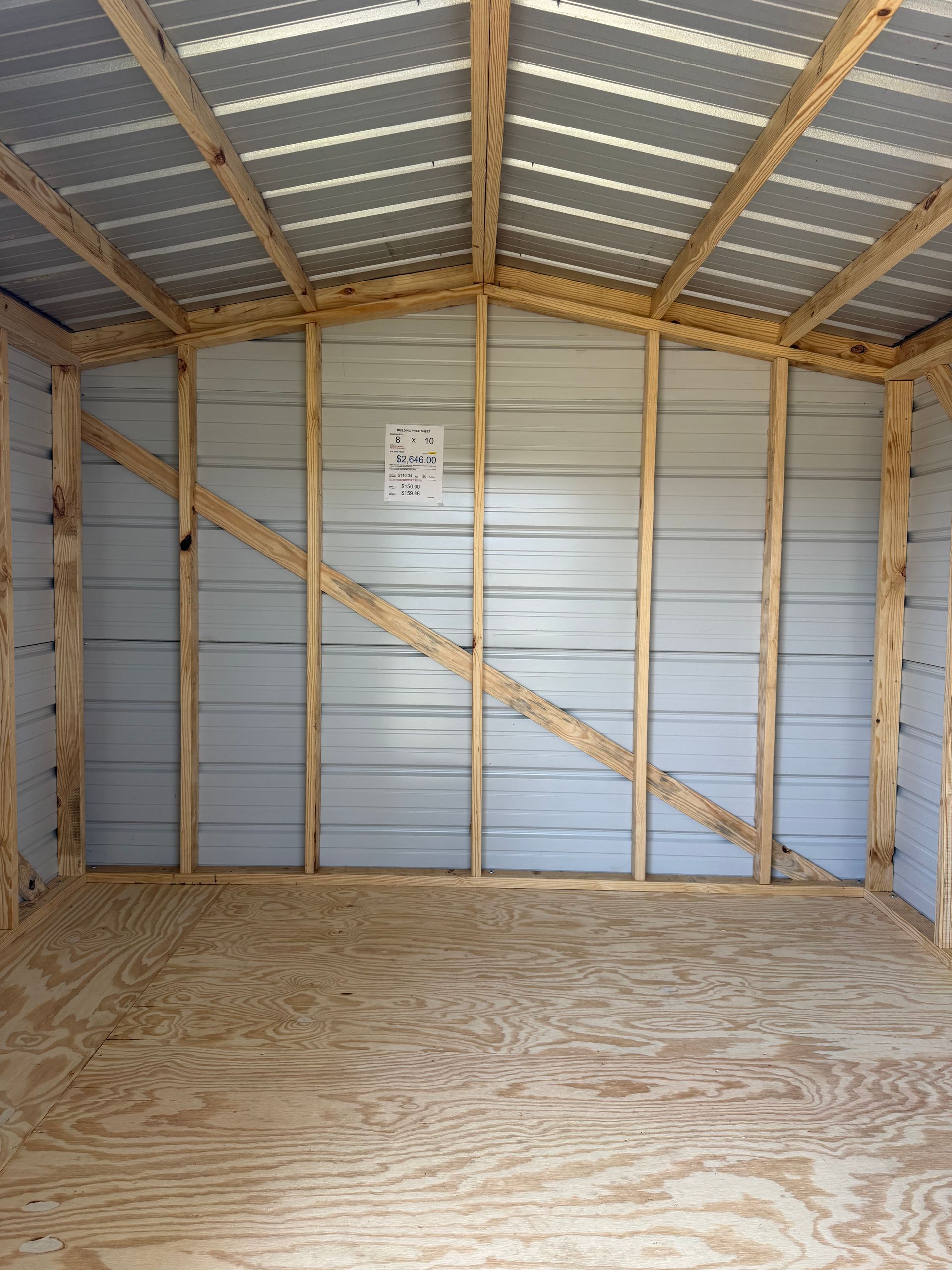 Empty shed interior with plywood floor, metal walls, and exposed wooden roof framing