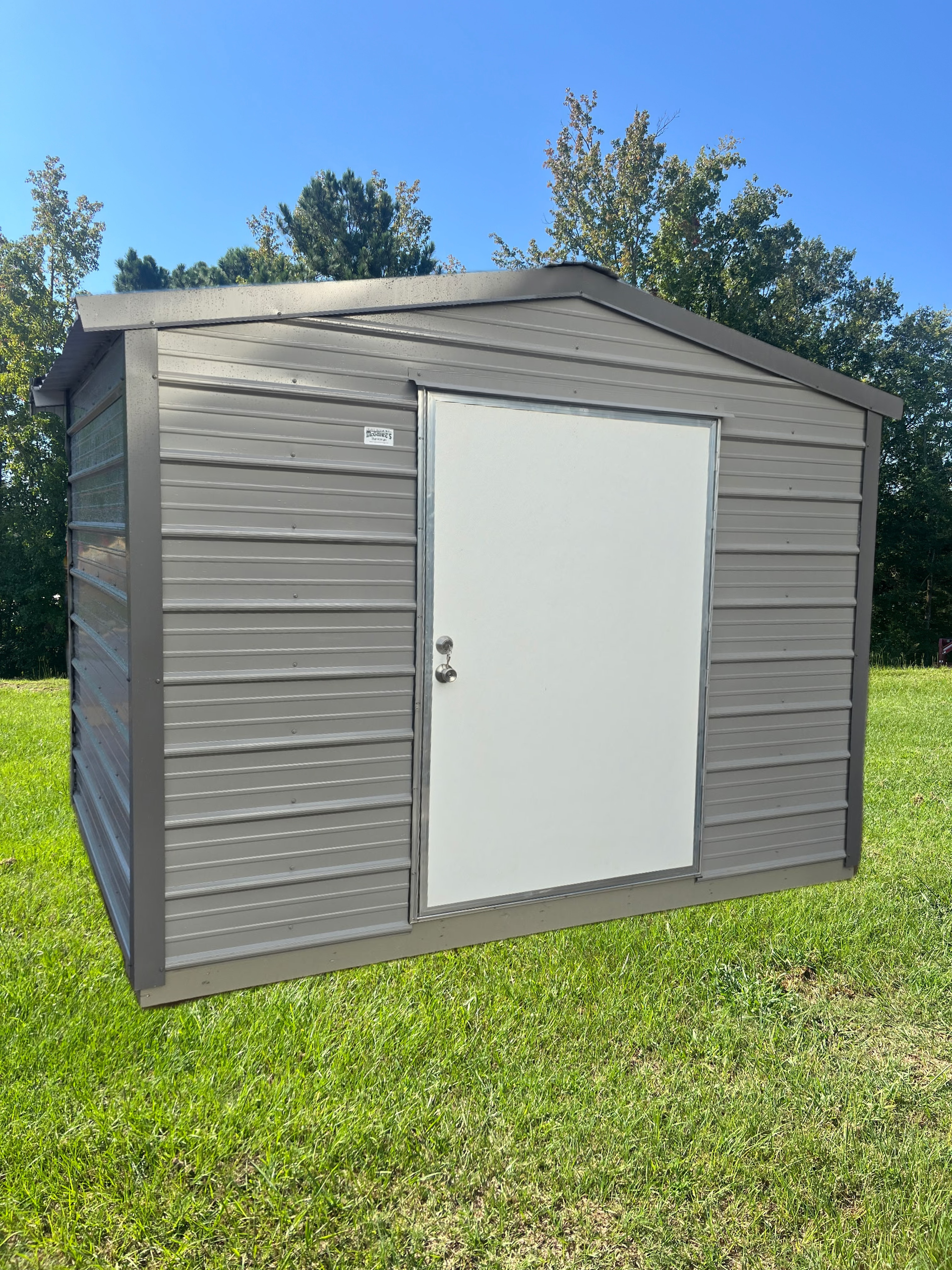 Gray outdoor storage shed with a white door on a grassy lawn under a blue sky