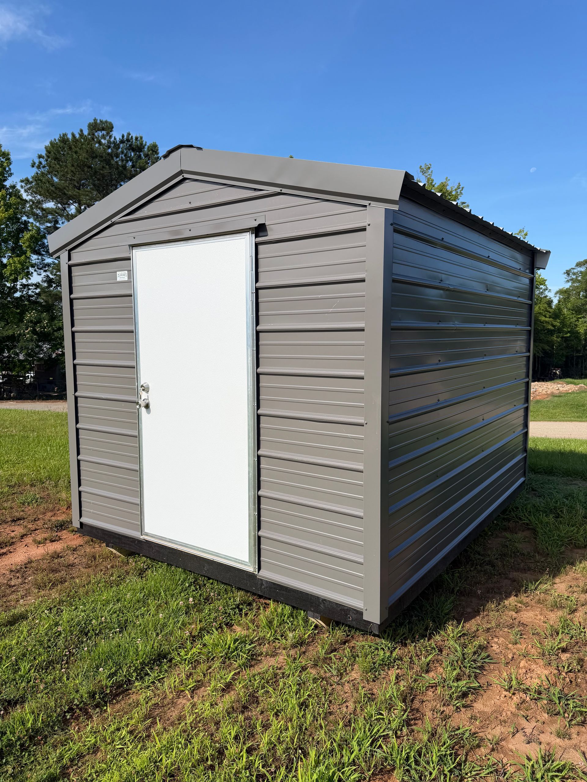 Gray outdoor storage shed with a white door on a grassy lawn under a blue sky