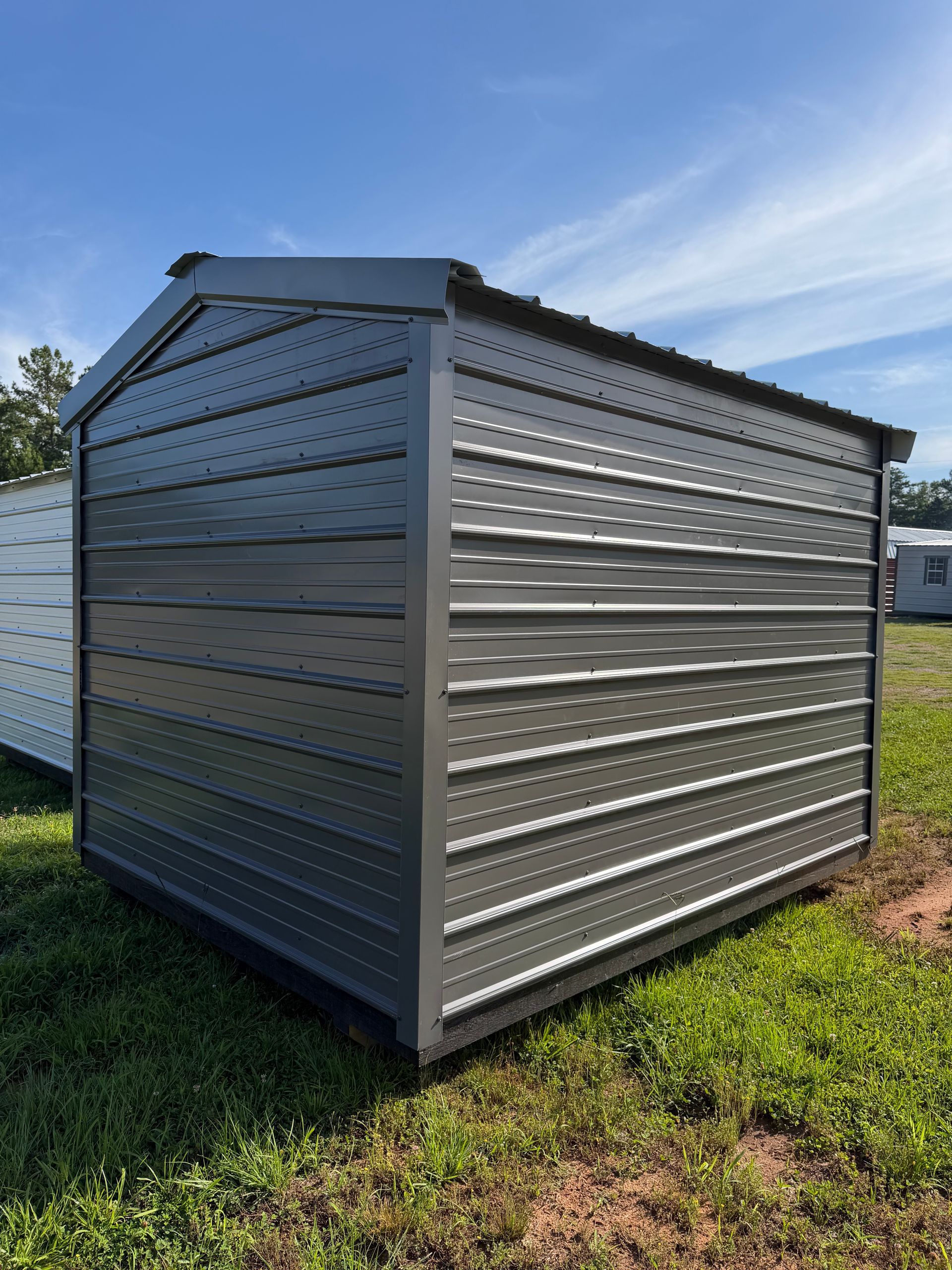 Gray metal storage shed with corrugated siding on a grassy lot under a blue sky
