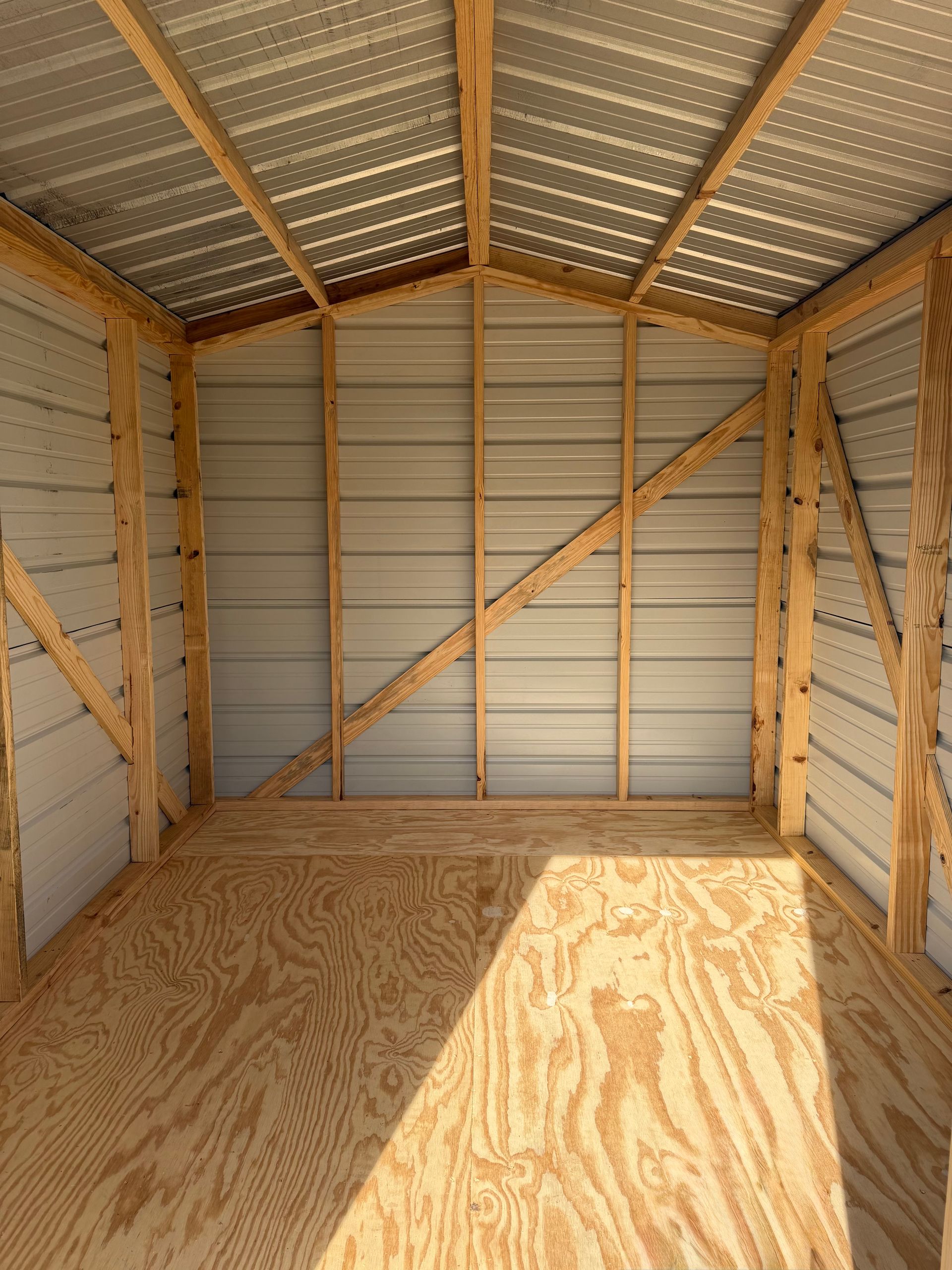 Empty plywood-walled storage shed with corrugated metal roof and bright sunlight on the floor