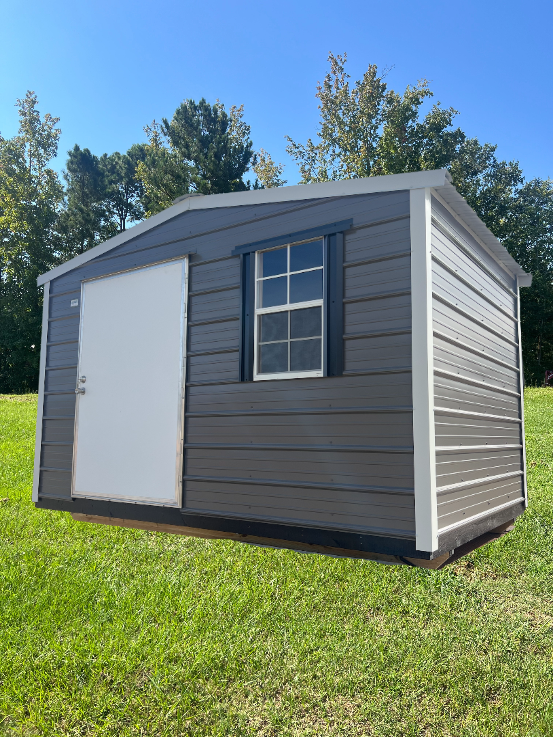 Gray shed with a white door and window on green grass under a blue sky.