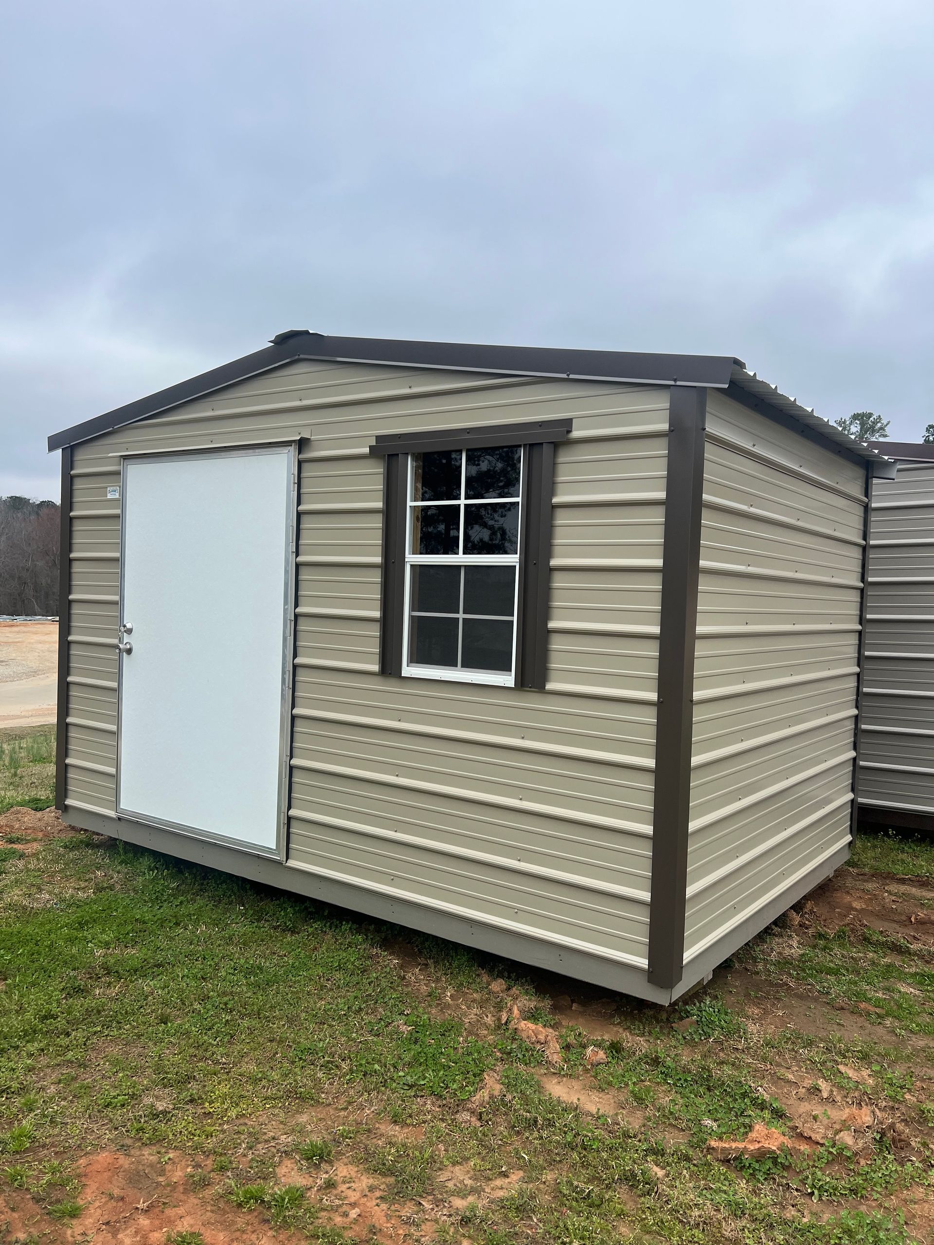 Tan and brown storage shed with a door and window, set on a grassy lawn with trees in the background.