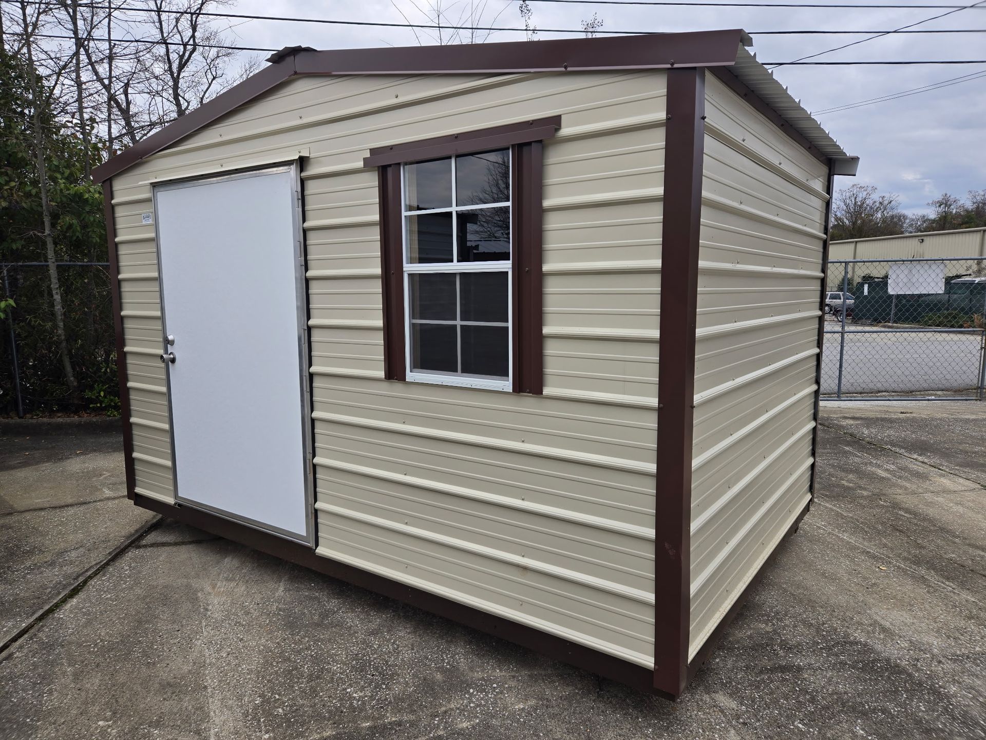 Tan shed with brown trim, door and window, on a concrete surface.