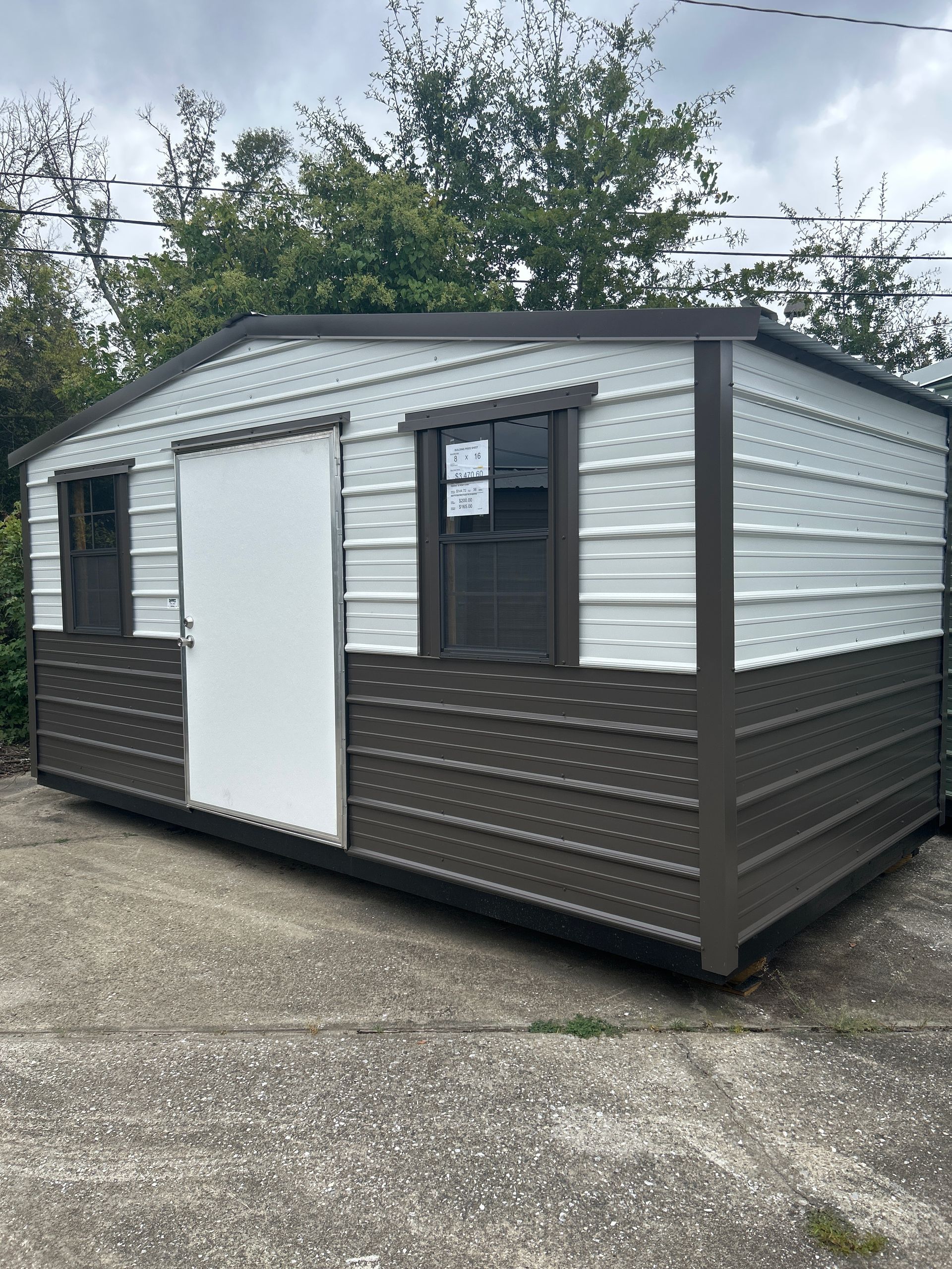 Metal shed with white and brown panels, two windows, and a door on a concrete surface.