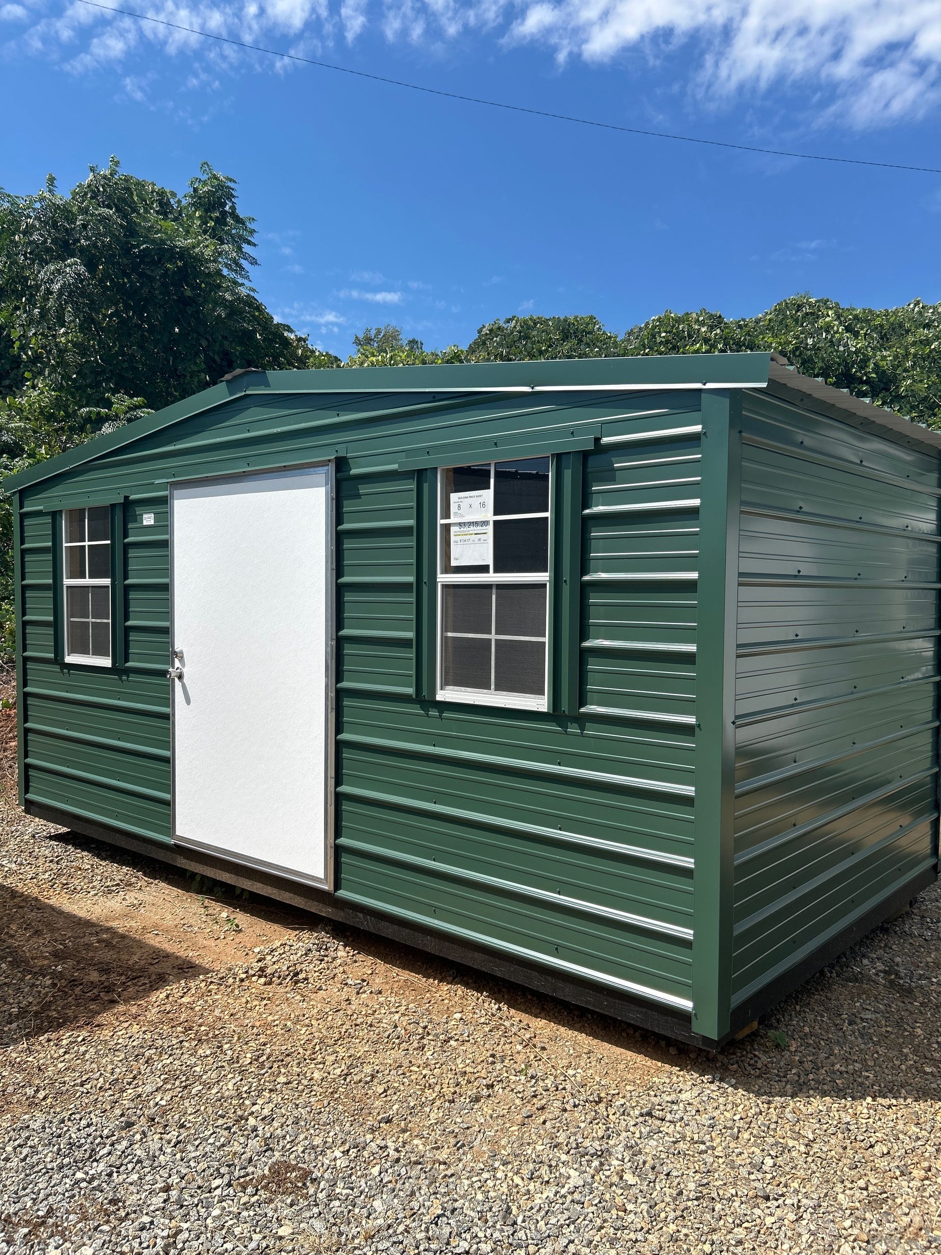 Green metal shed with a white door and windows under a blue sky.