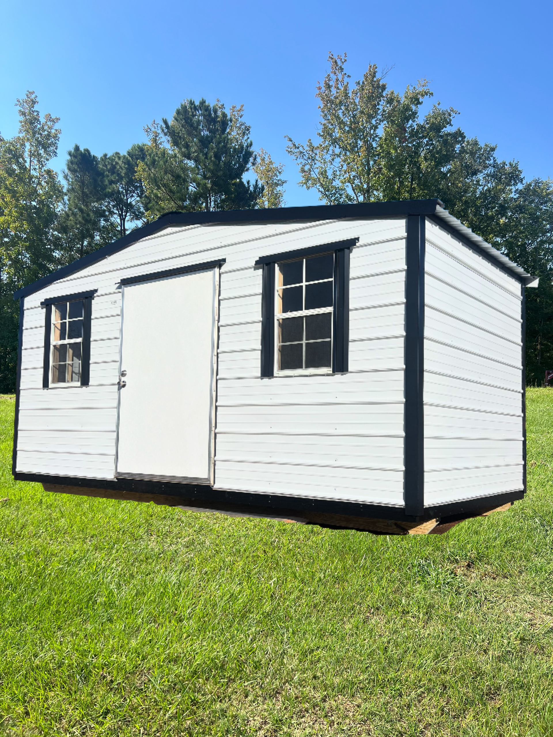 White shed with black trim and two windows on green grass.