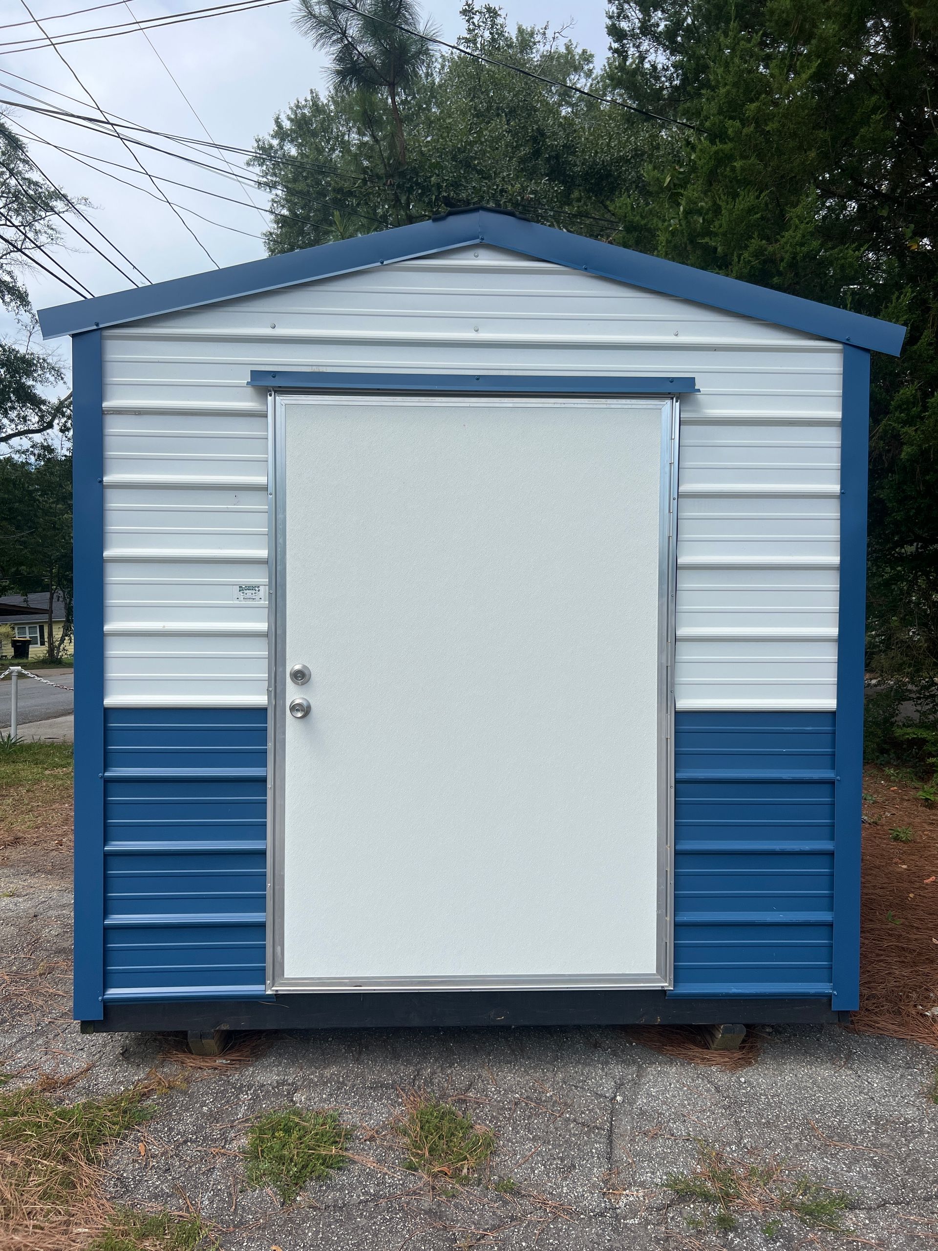 Blue and white storage shed with a white door, set on gravel.