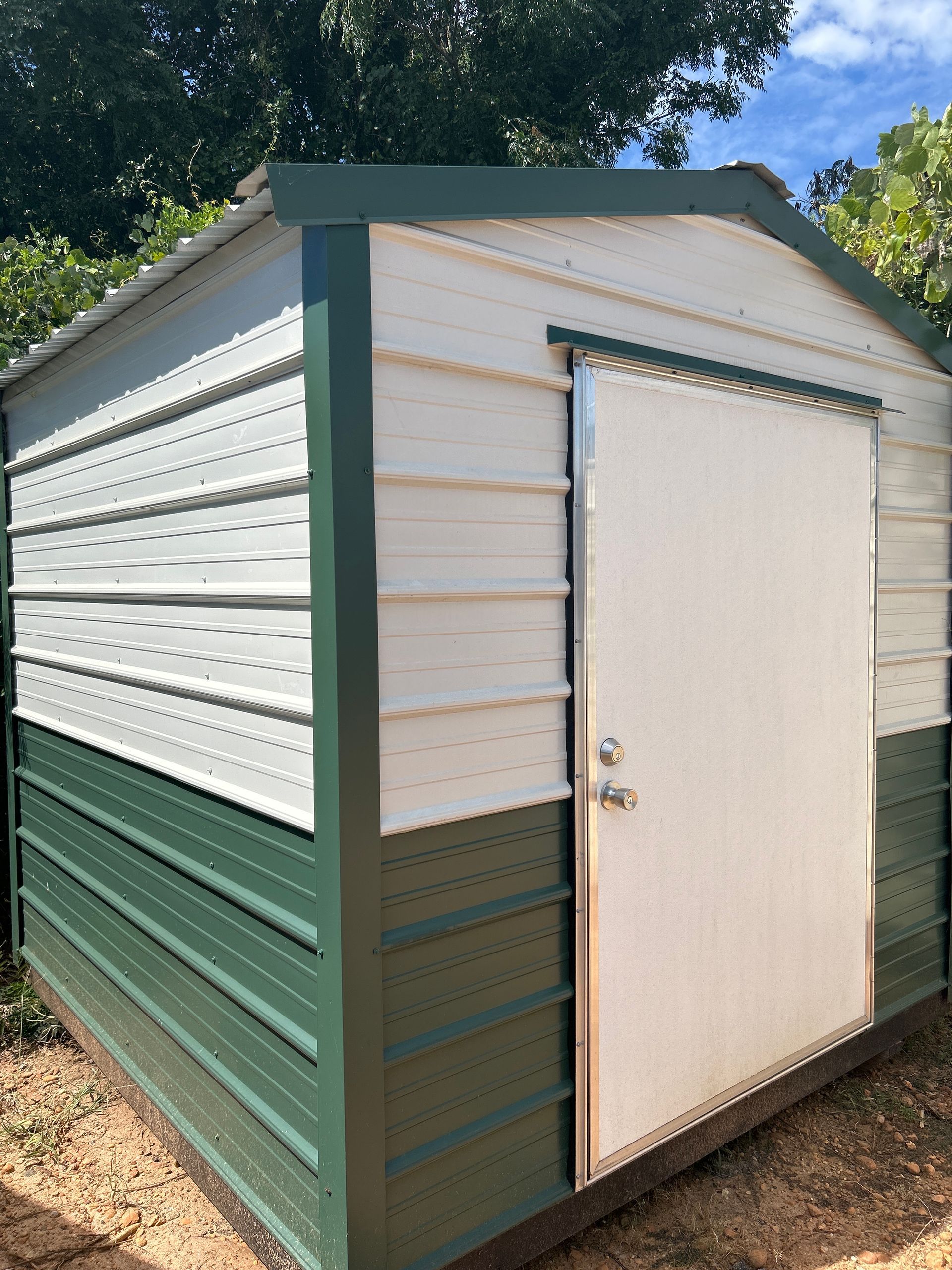 Green and white storage shed with a white door, set outside under a blue sky.