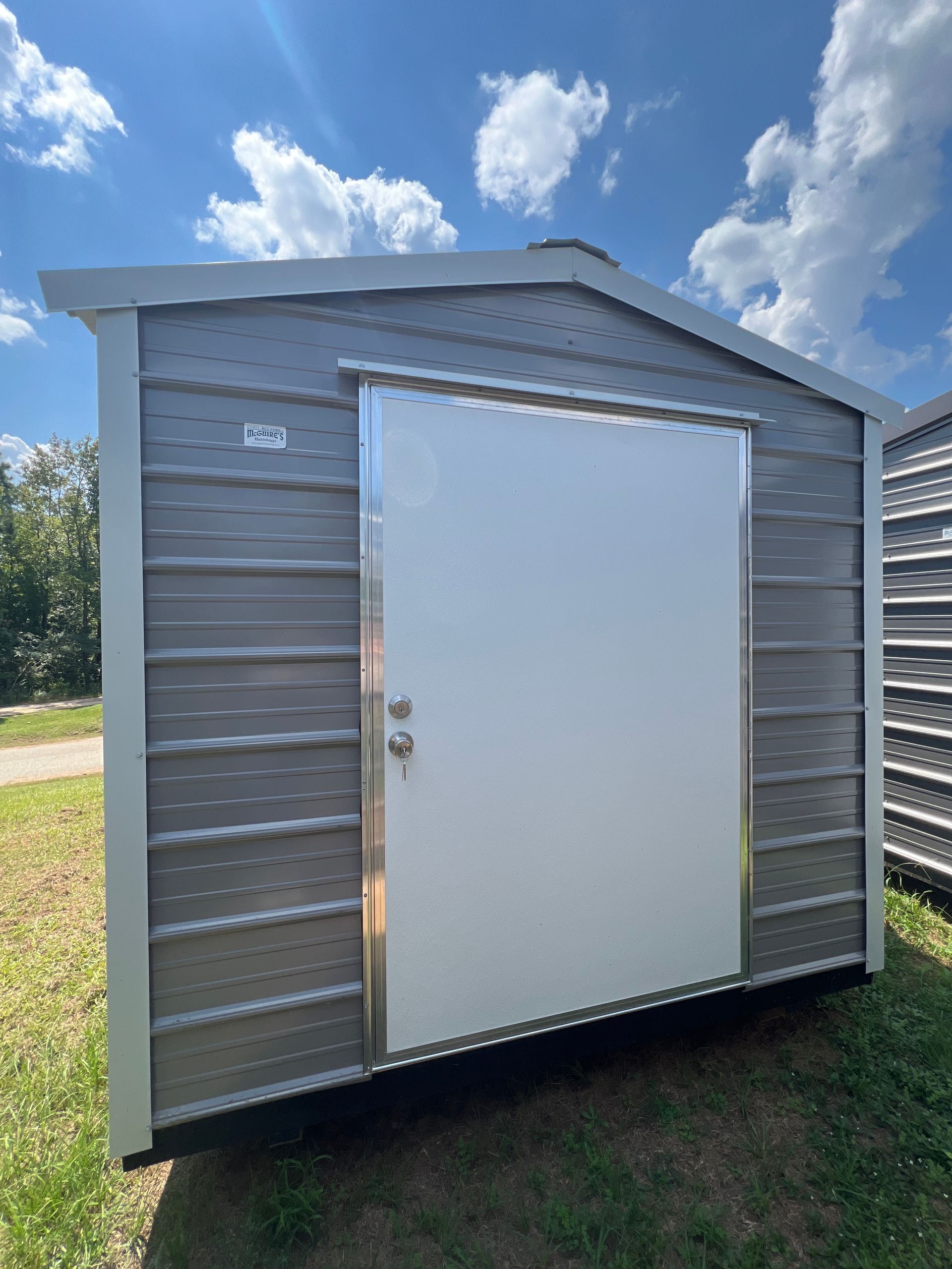 Gray shed with white door, silver trim, and light blue sky background.