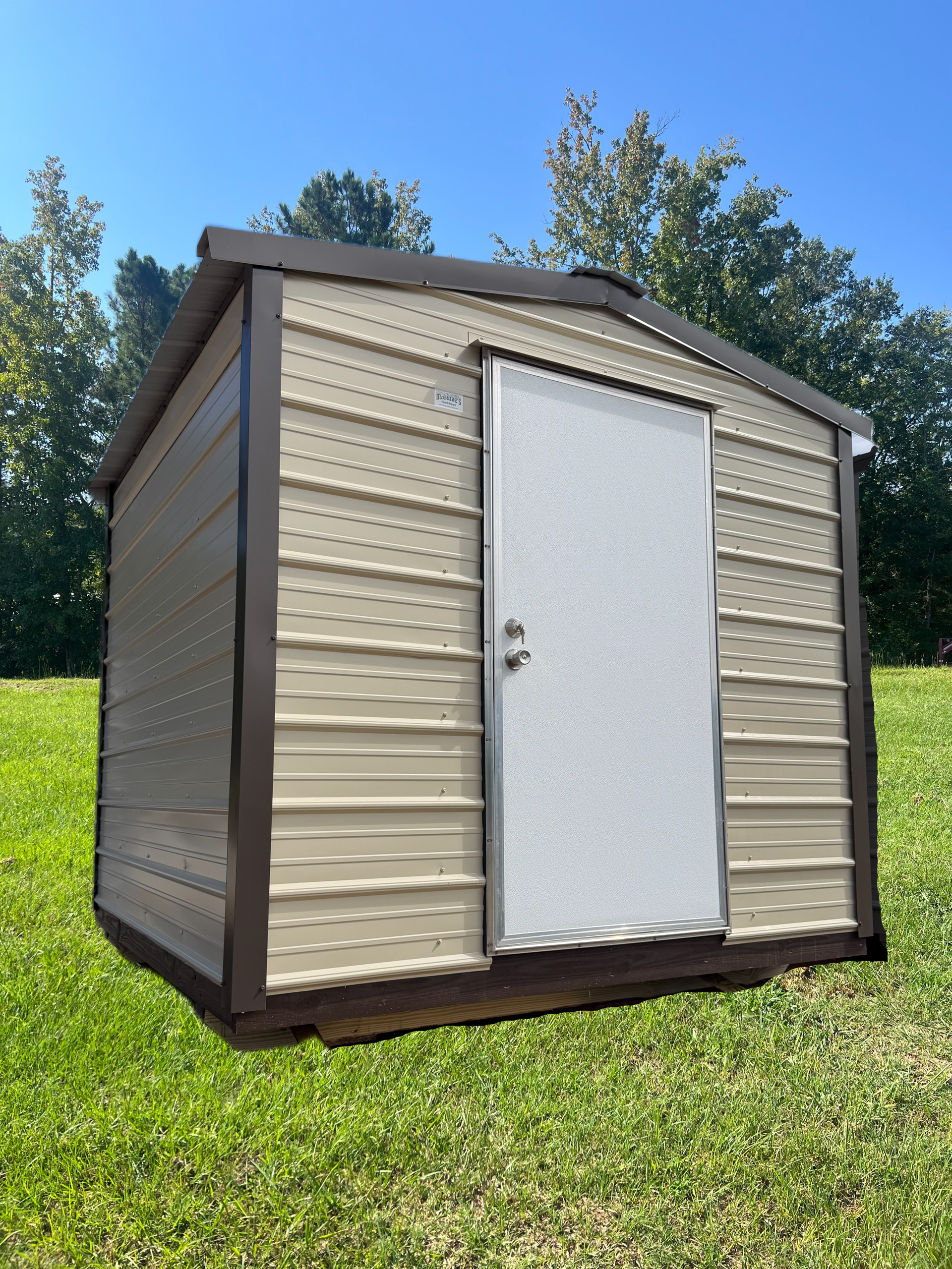 Small beige and brown storage shed with a white door, sitting on green grass under a blue sky.