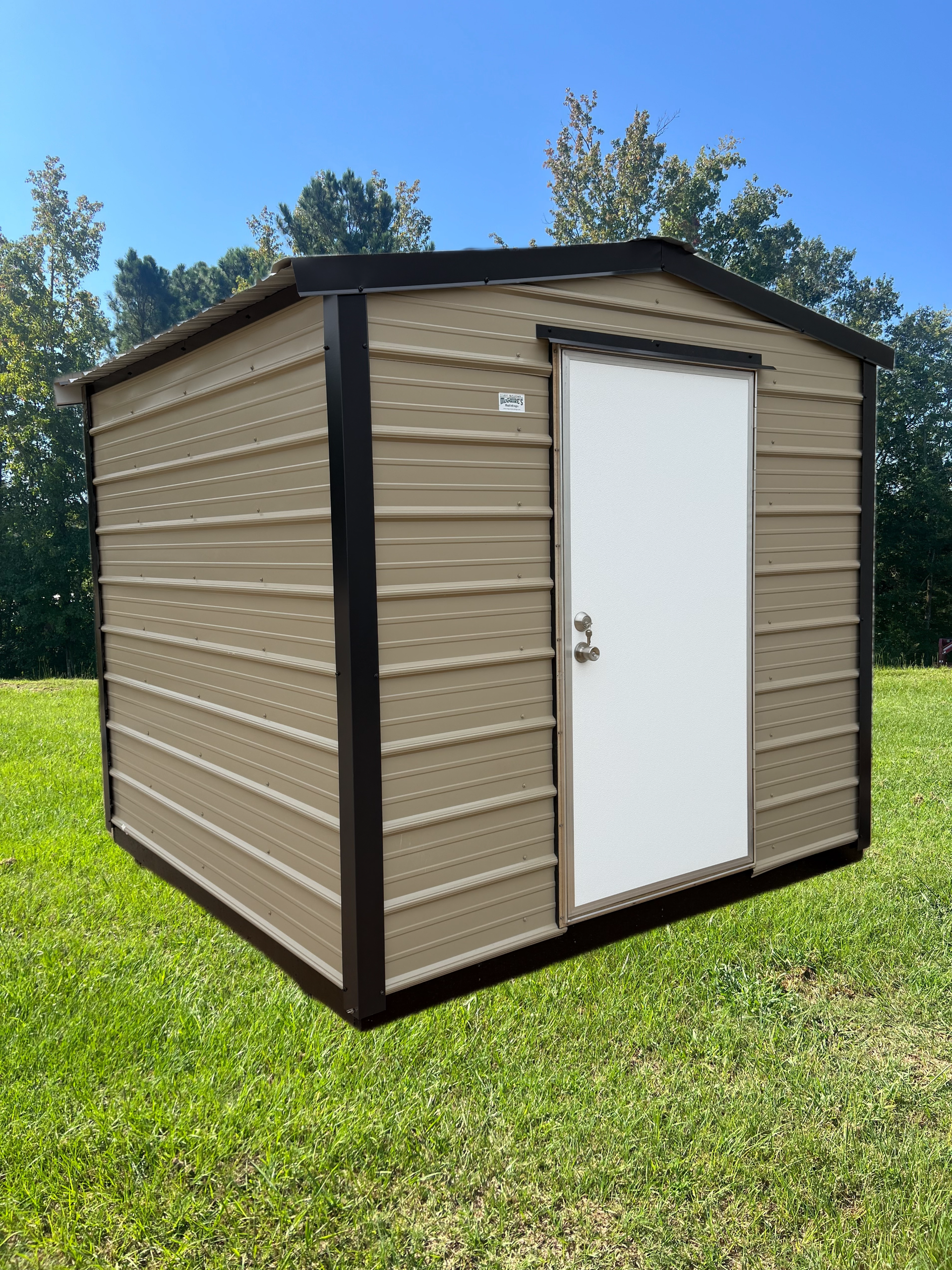 Small tan shed with white door and dark trim standing on grass under a blue sky