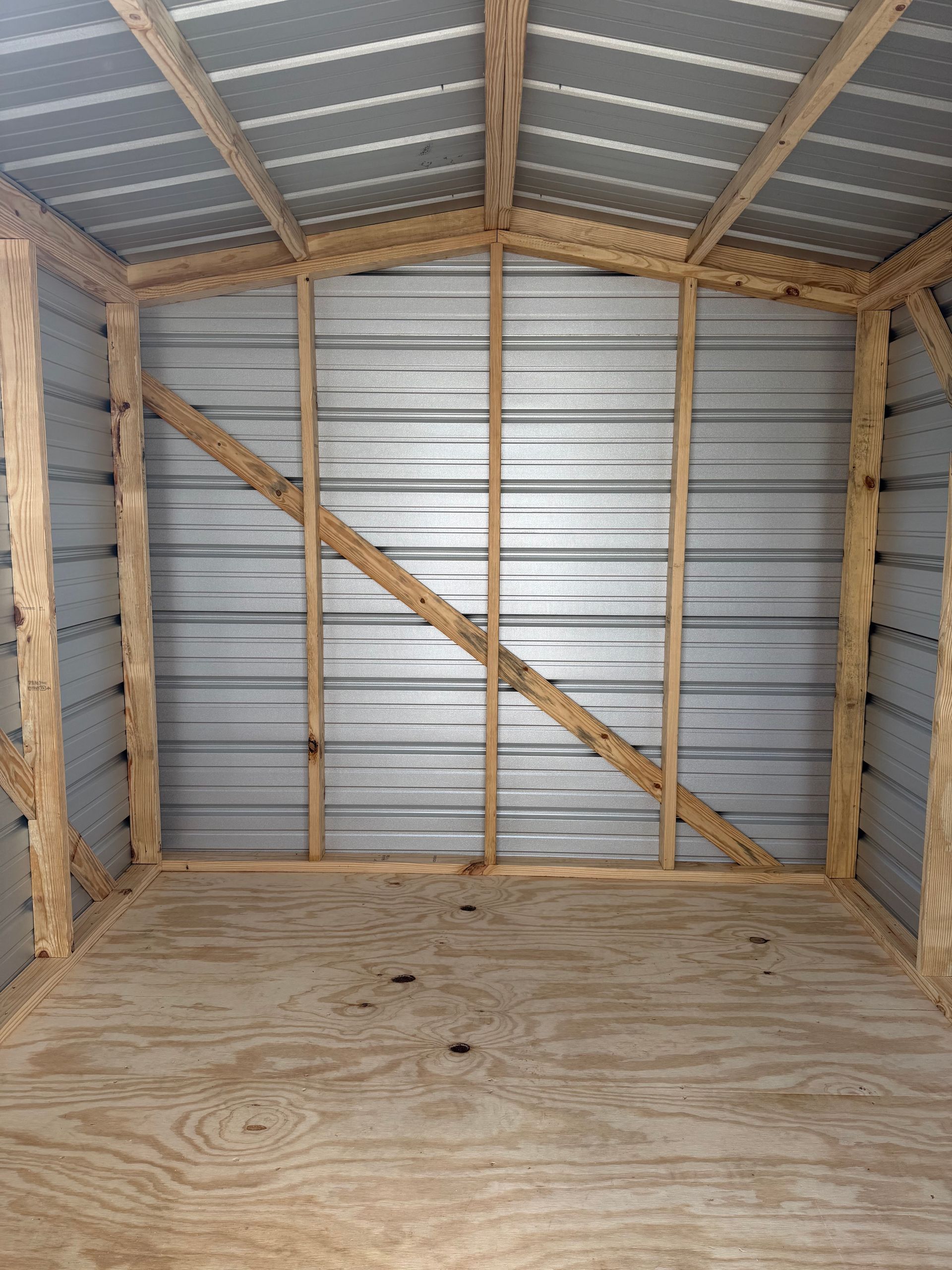 Empty metal shed interior with plywood floor, corrugated walls, and diagonal wooden supports