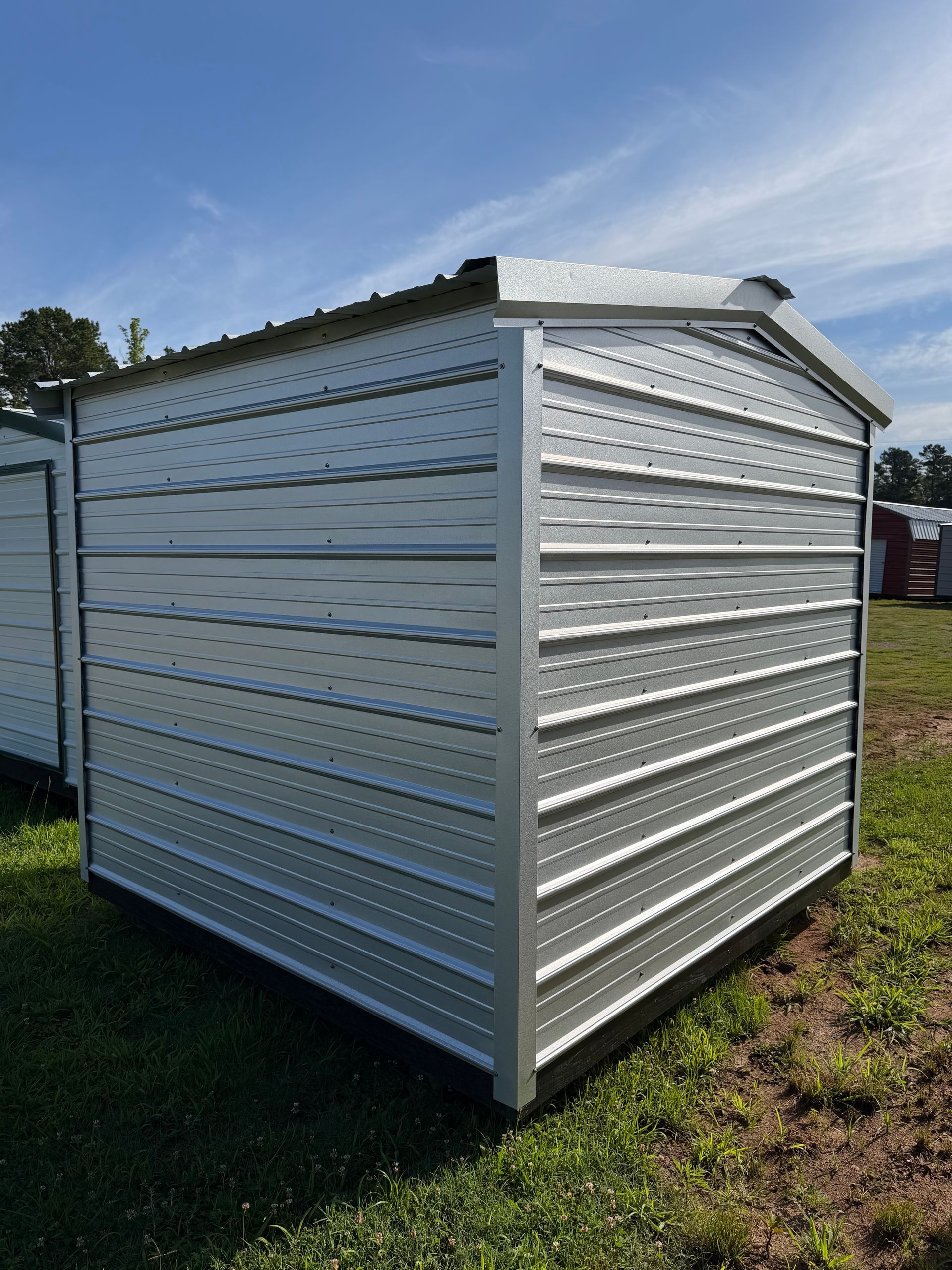 Small white metal storage shed with a sloped roof on grass under a blue sky