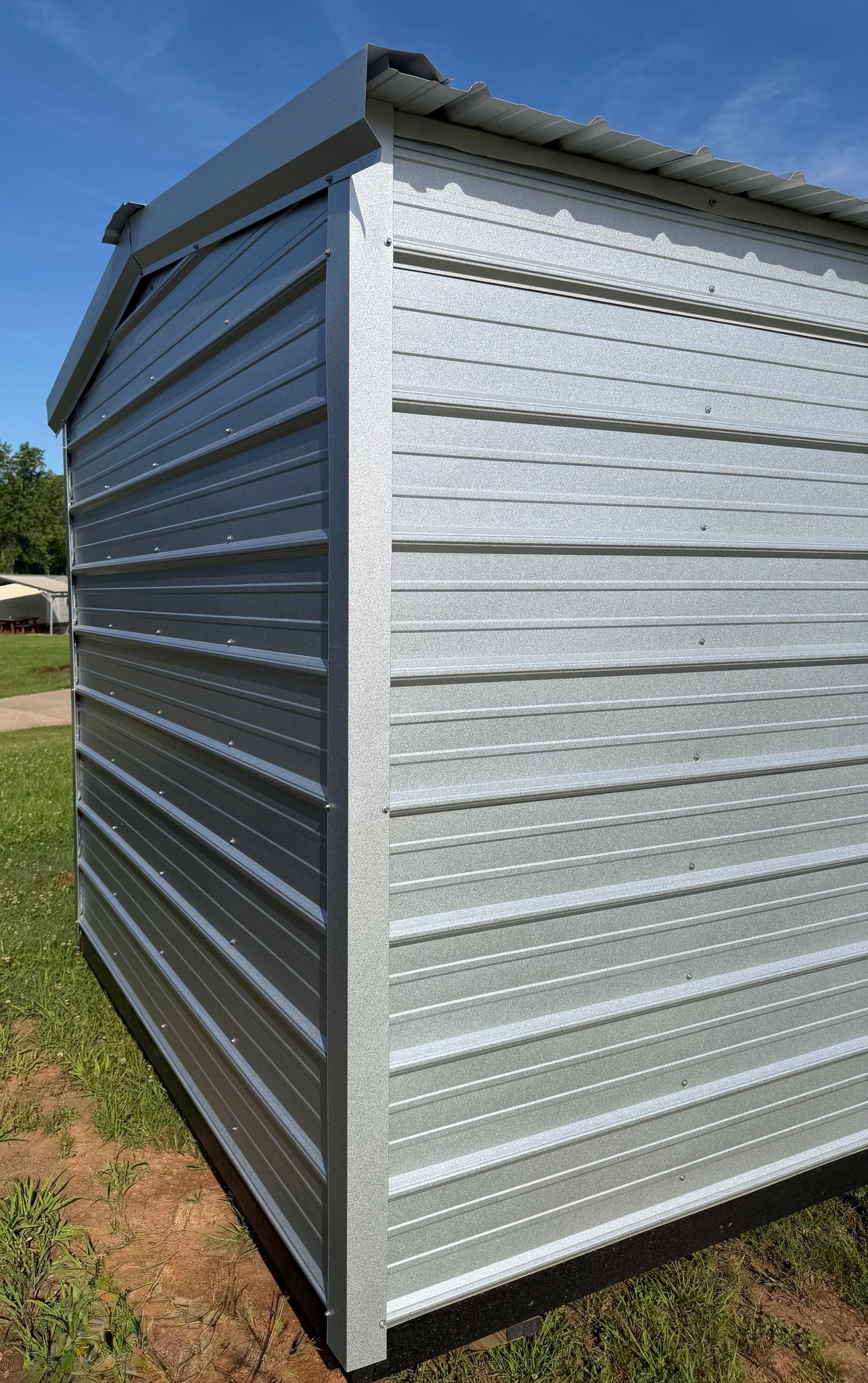 Silver metal storage shed with corrugated walls and a slanted roof on a grassy yard