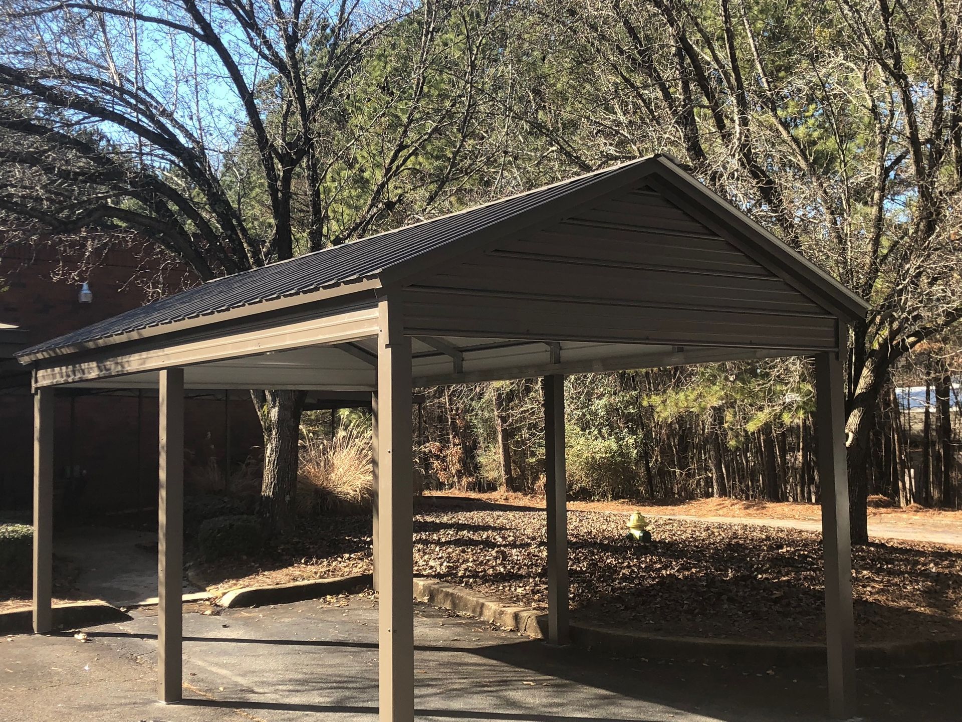 Brown metal carport with corrugated roof, in front of trees.