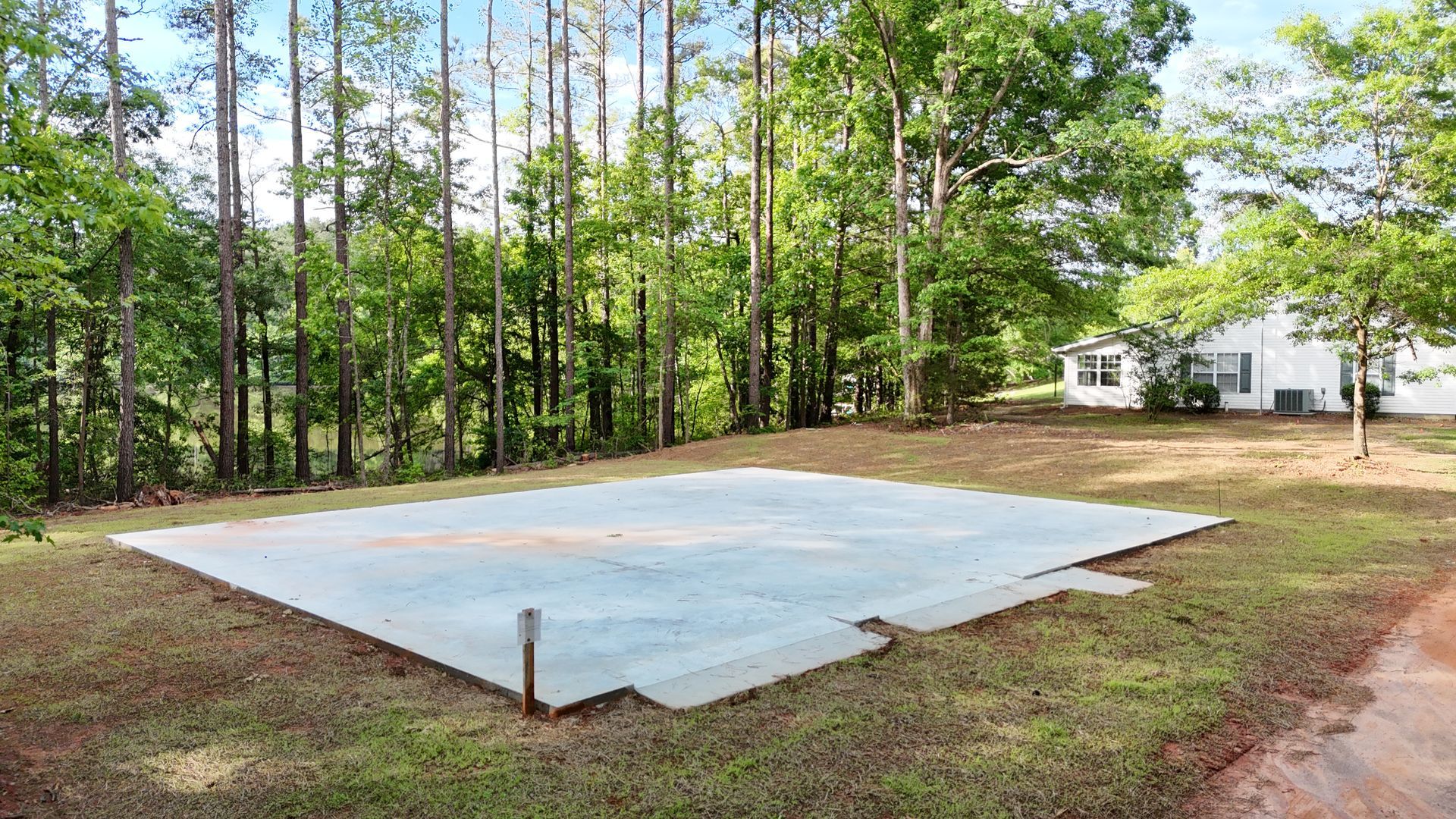 Concrete slab in a grassy yard, surrounded by trees and a white house in the background.