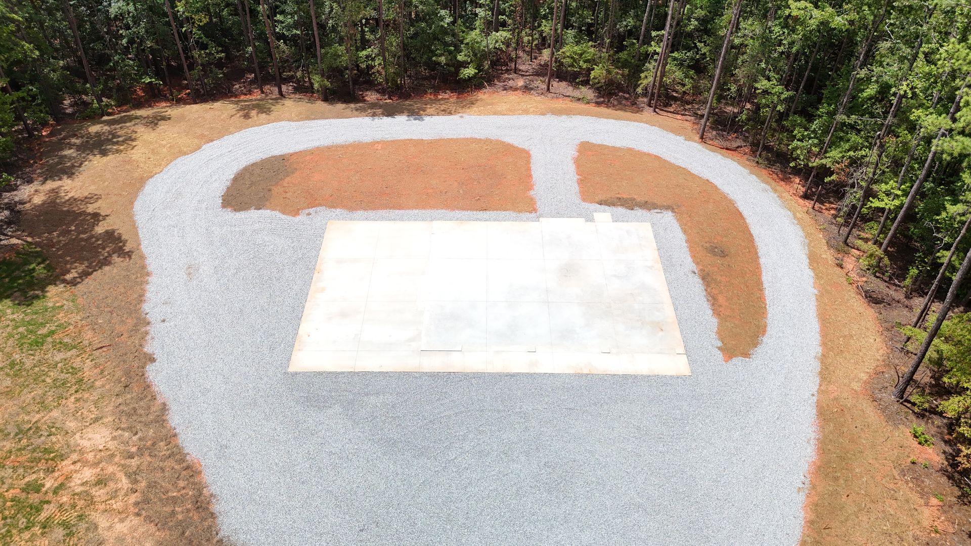 Concrete pad surrounded by gravel and dirt, in a clearing near trees.