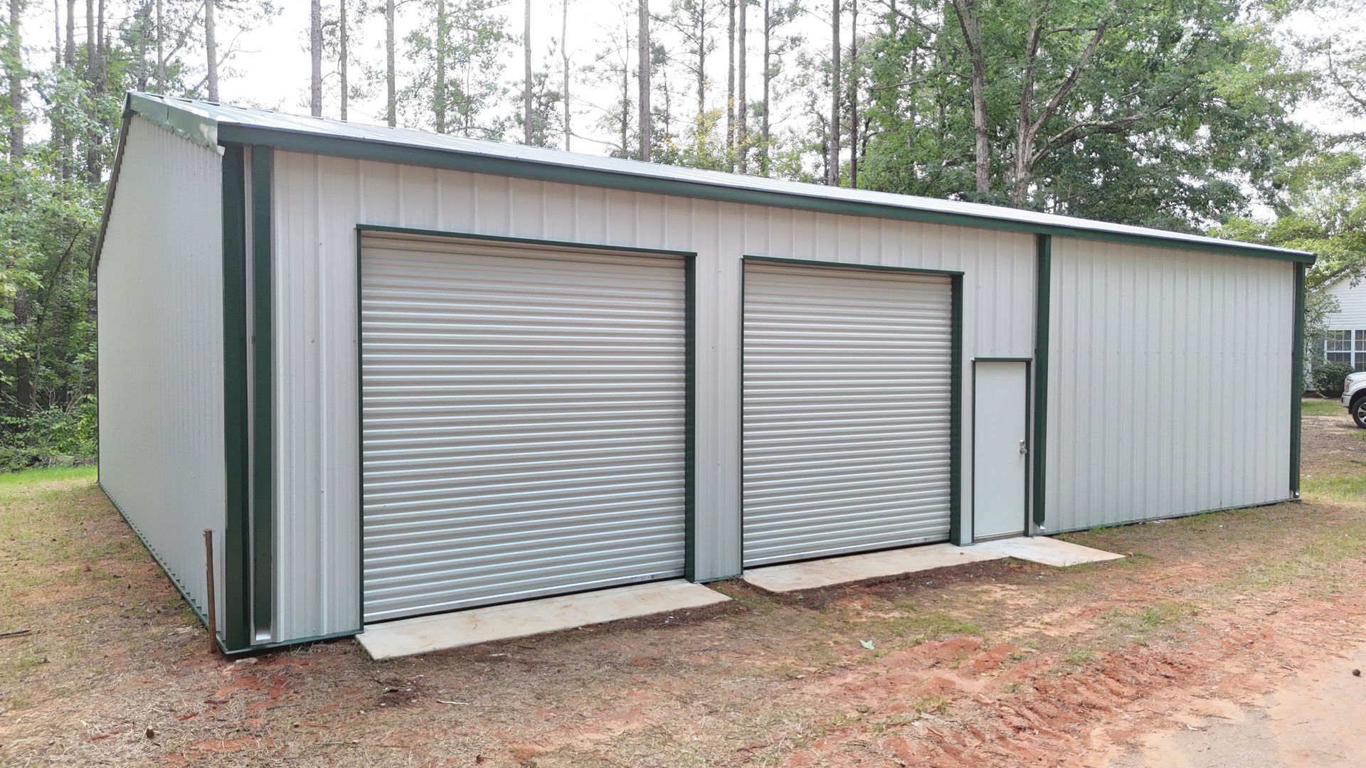 A metal garage with two large roll-up doors and a small side door; green trim and a light gray exterior.