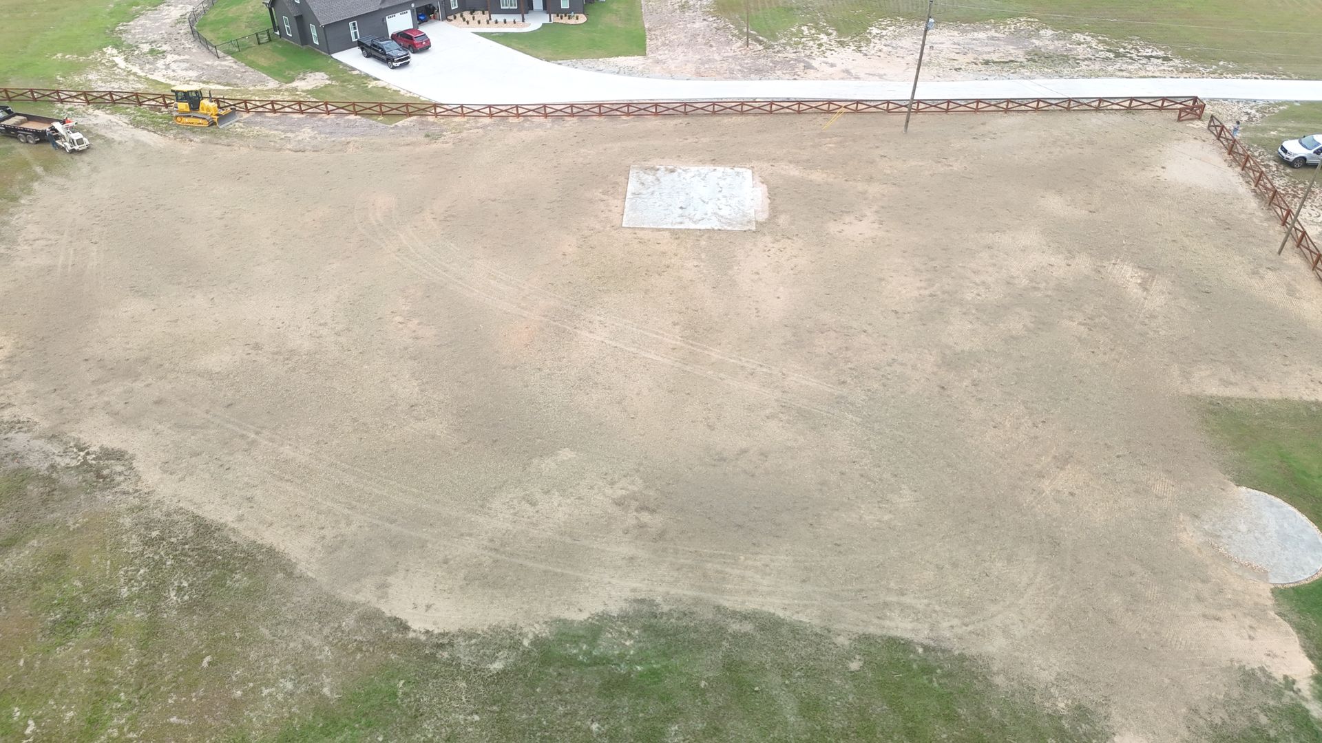 Aerial view of a cleared dirt lot with a small building and some construction equipment visible.